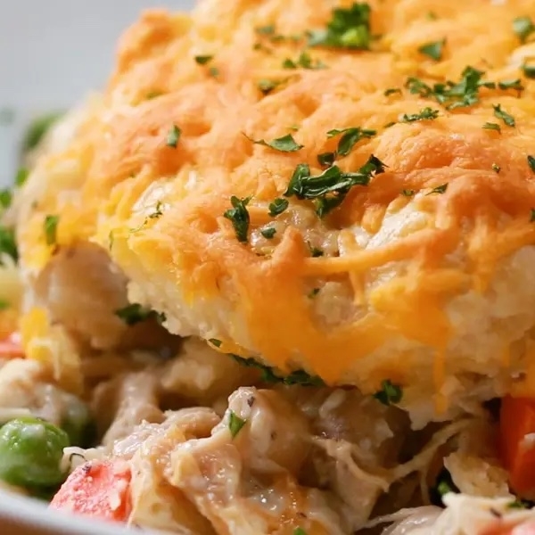 Closeup of a cheesy, baked dish with chicken, peas, and carrots, topped with parsley