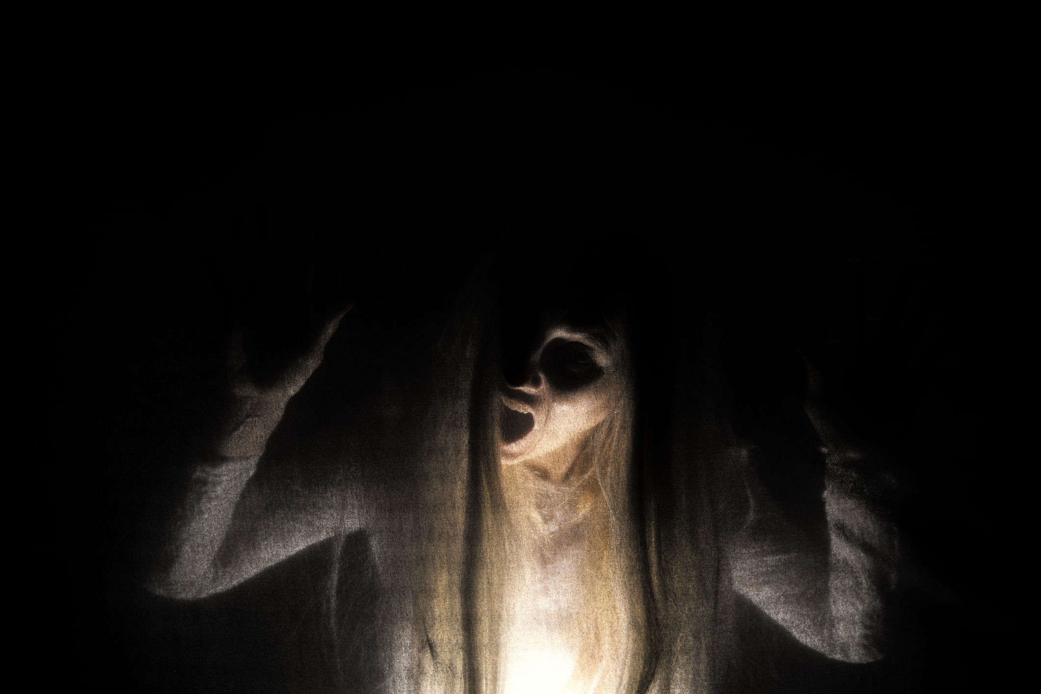 A ghostly figure with long hair in the dark and illuminated by a light