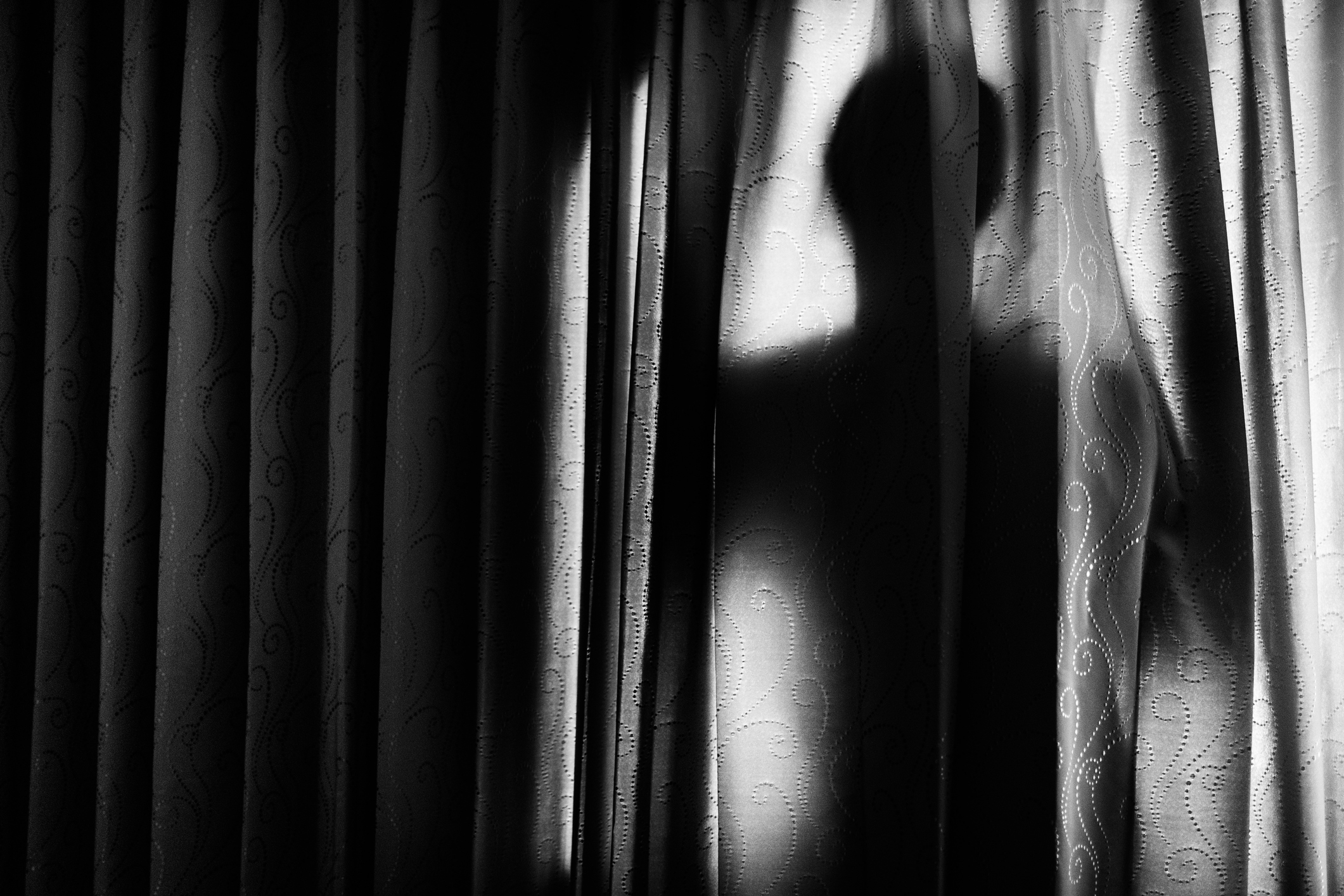 Silhouette of a figure peering through curtains