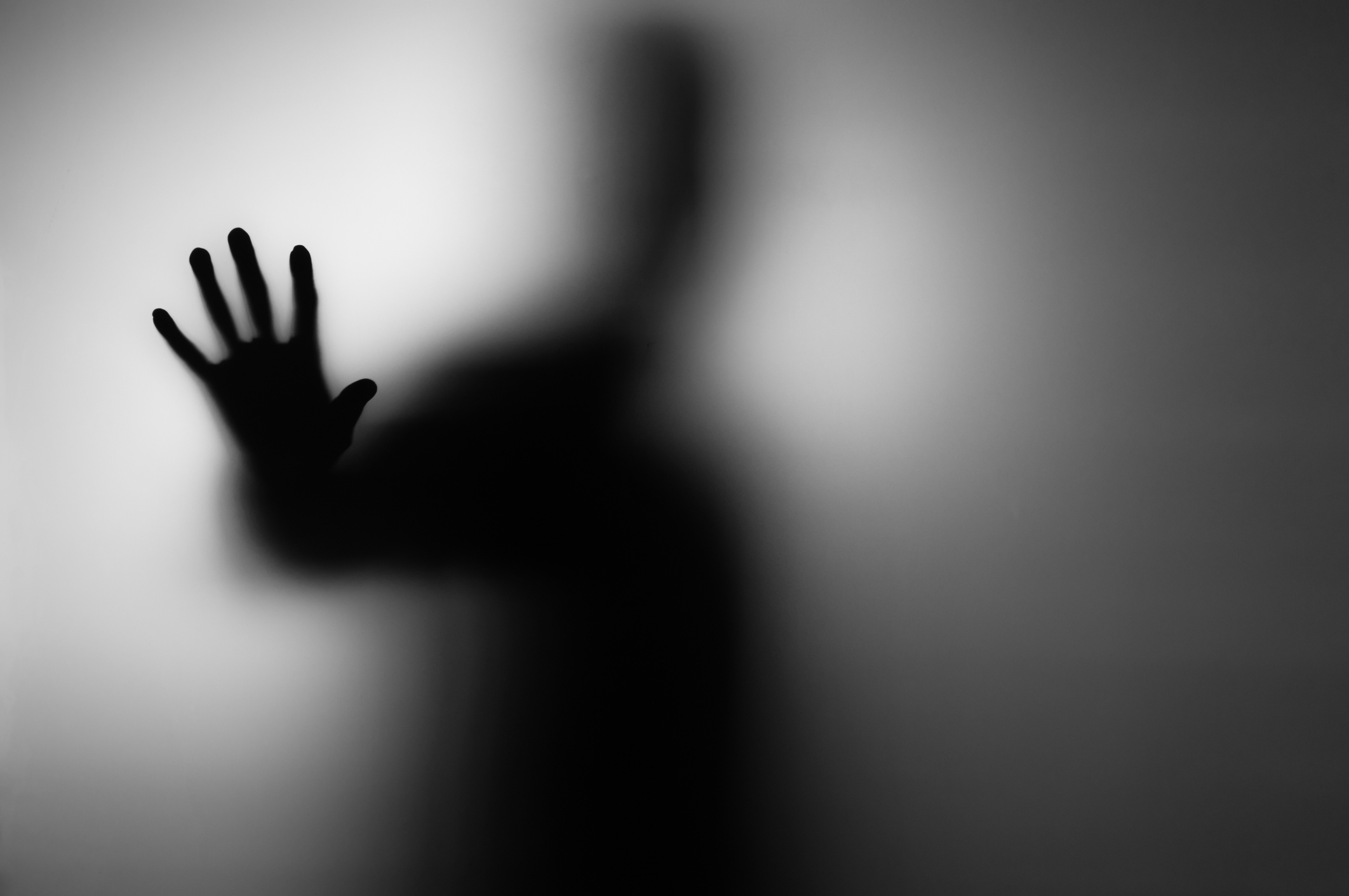 A blurry silhouette of a person holding their hand up against a translucent barrier