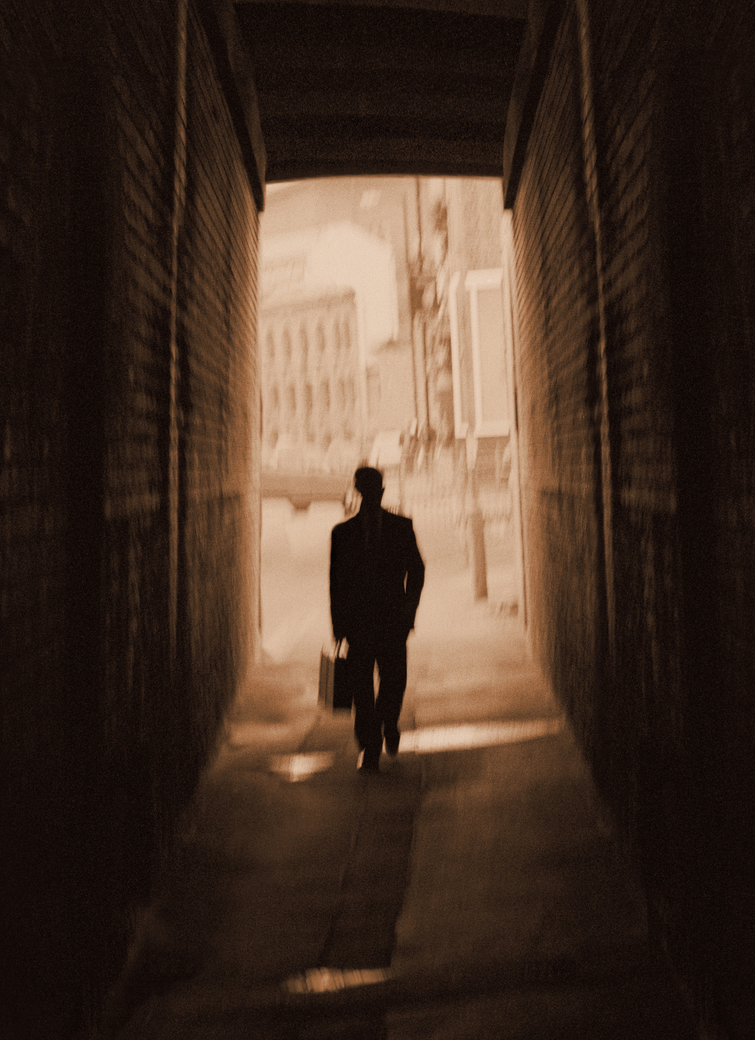 A person in a suit and pants and a briefcase walking down a narrow dark pathway