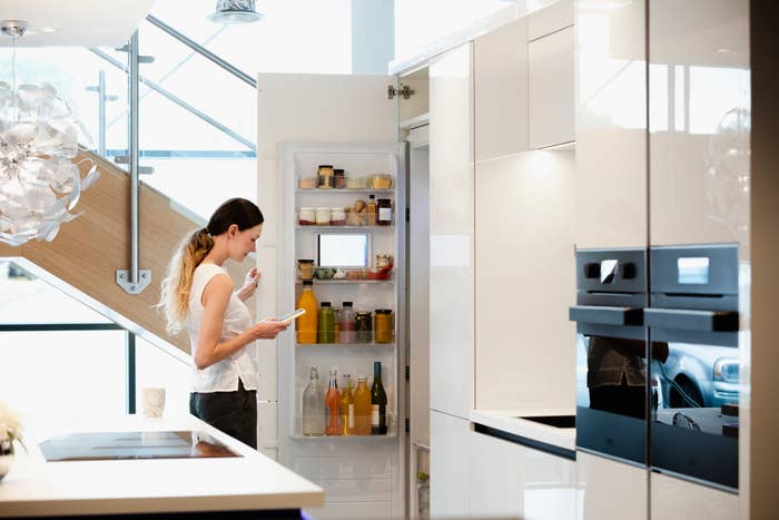 a woman is reaching into her smart fridge for a snack