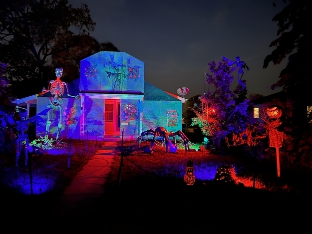 A house at night with dramatic lights along with skeletons, a large spider, and pumpkin head in the front yard