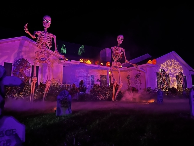 Two skeletons in front of a house at night with gravestones in the grass