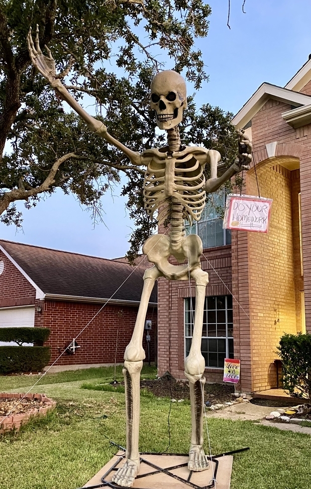 A skeleton in front of a house with a &quot;Do your homework&quot; sign hanging off it