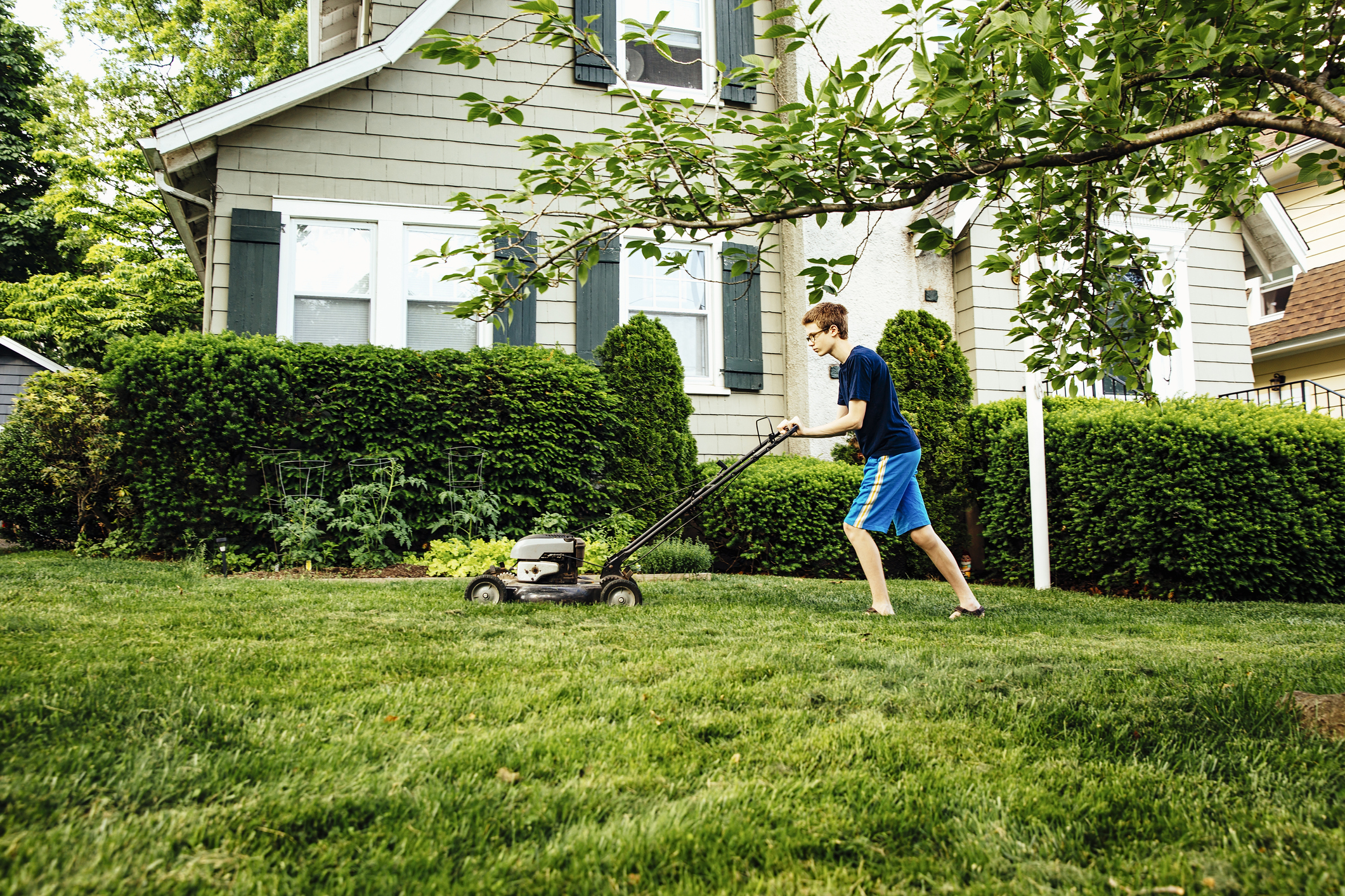 A teenage boy is mowing the lawn