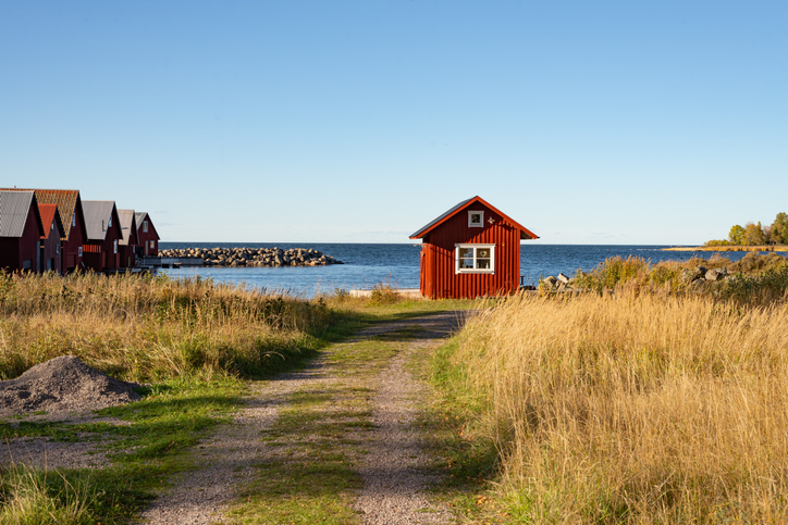 A small red shack amid tall grass by the water at the end of a country road