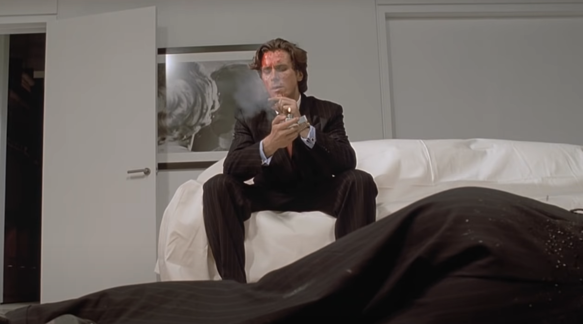 Patrick Bateman, played by Christian Bale, sitting on a couch and smoking a cigar