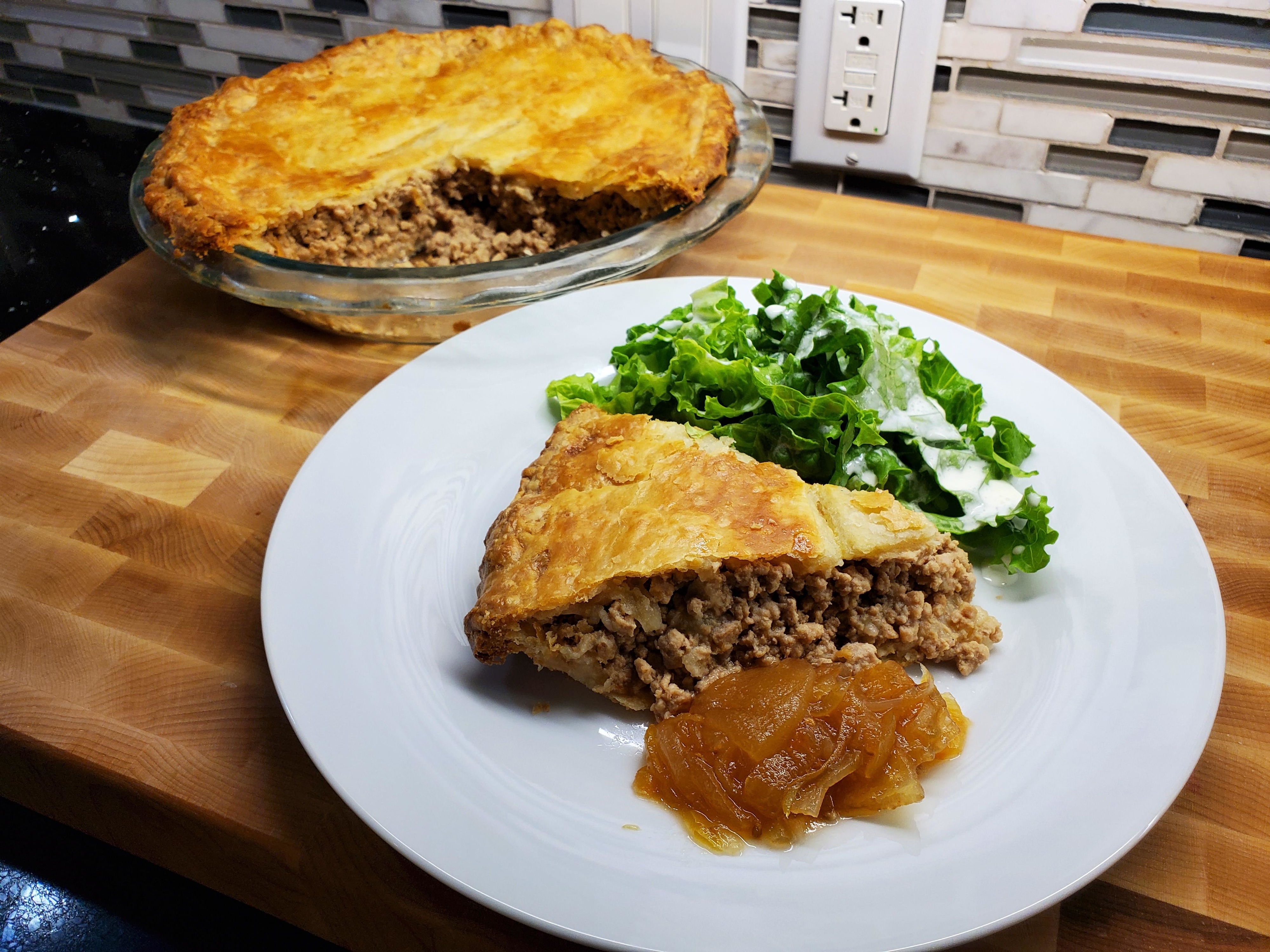 A slice of tourtière on a plate next to a leafy salad