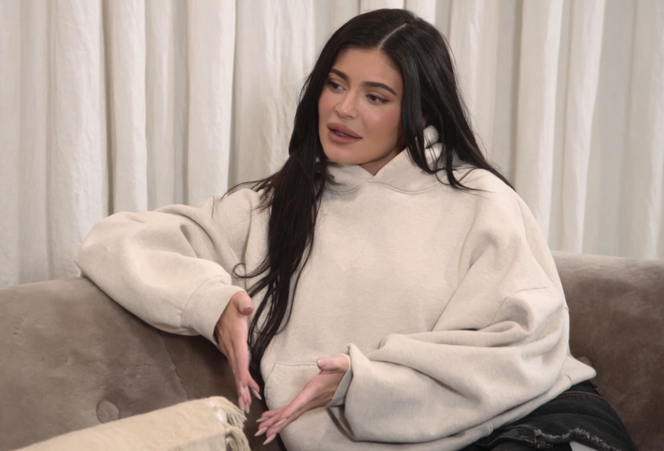 Close-up of Kylie sitting on a couch and wearing an oversize, long-sleeved hoodie