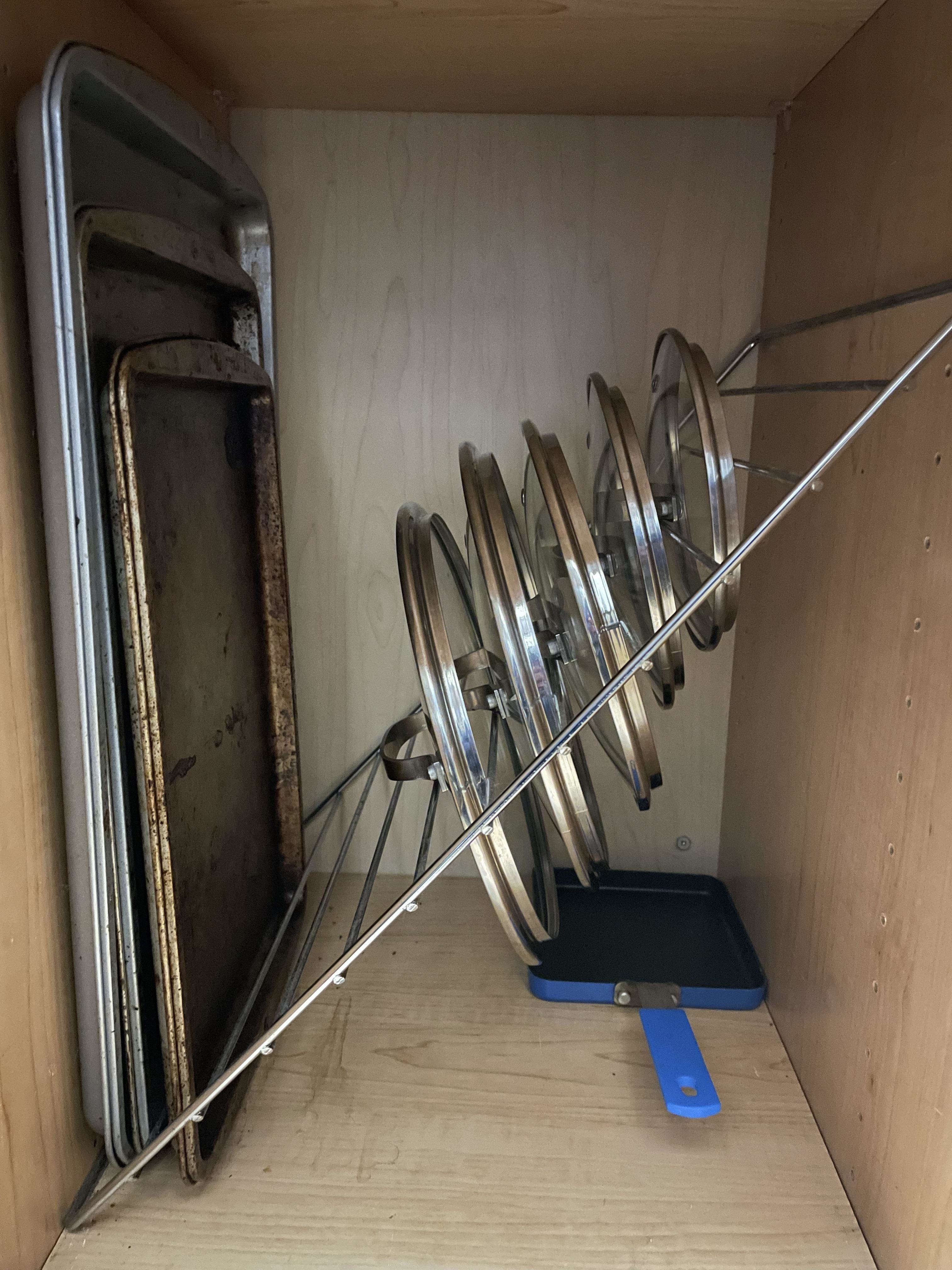 Pot and pan lids stacked diagonally in a cabinet on a wire oven rack