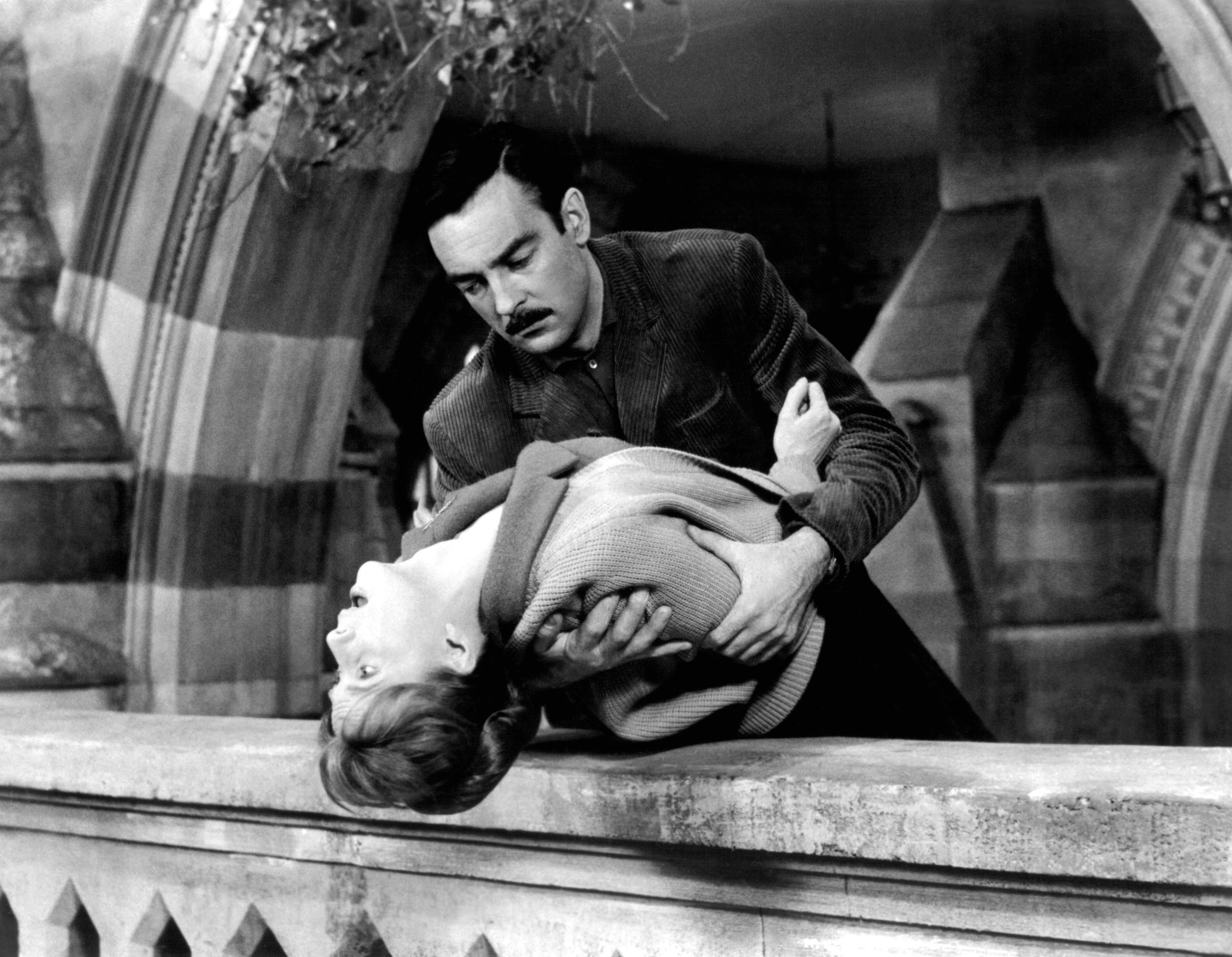 A man, Richard Johnson playing Dr John Markway, holds a woman, Julie Harris playing Eleanor, over a balcony