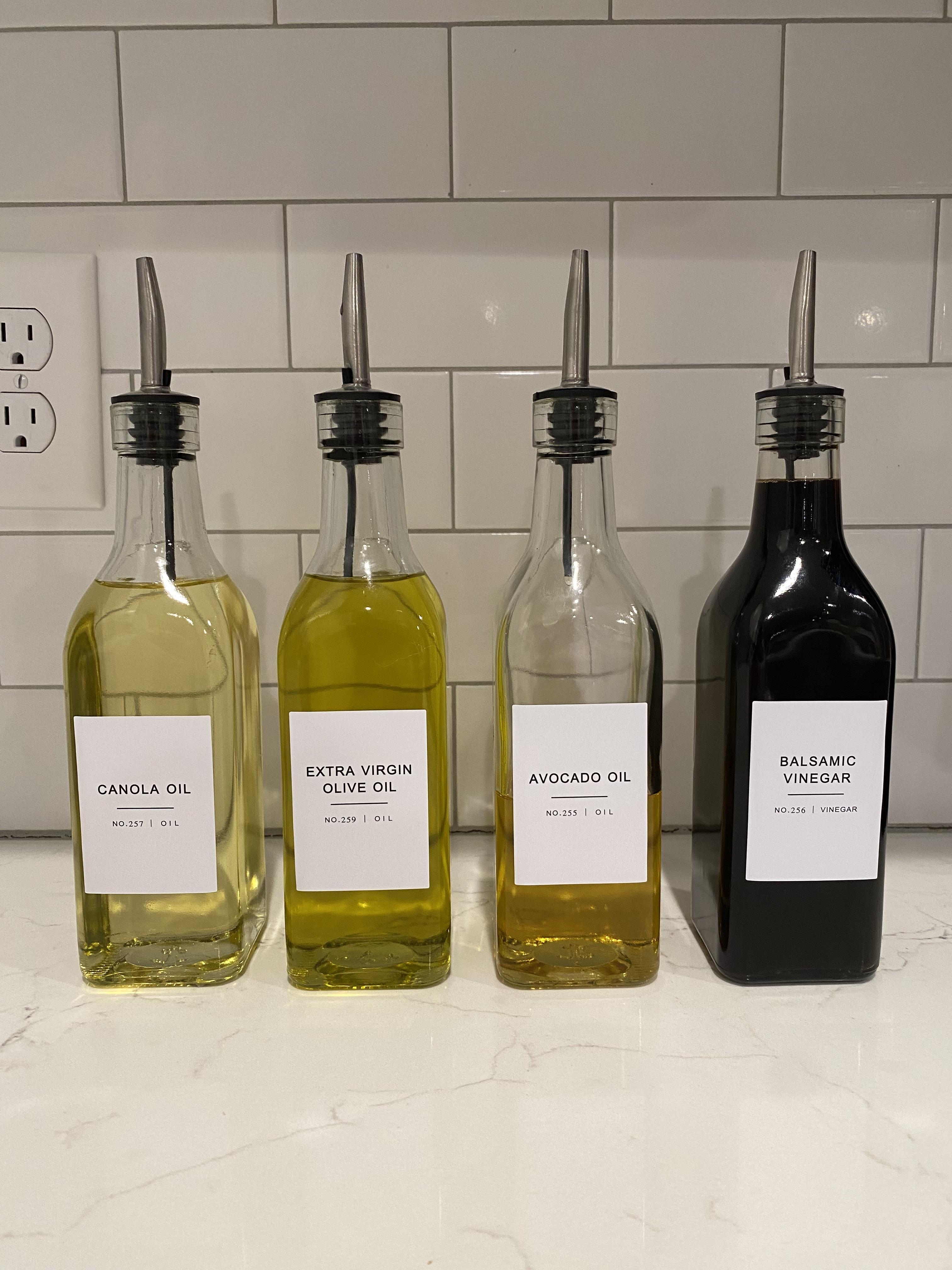 Glass bottles in the kitchen labeled for canola oil, olive oil, avocado oil, and balsamic vinegar