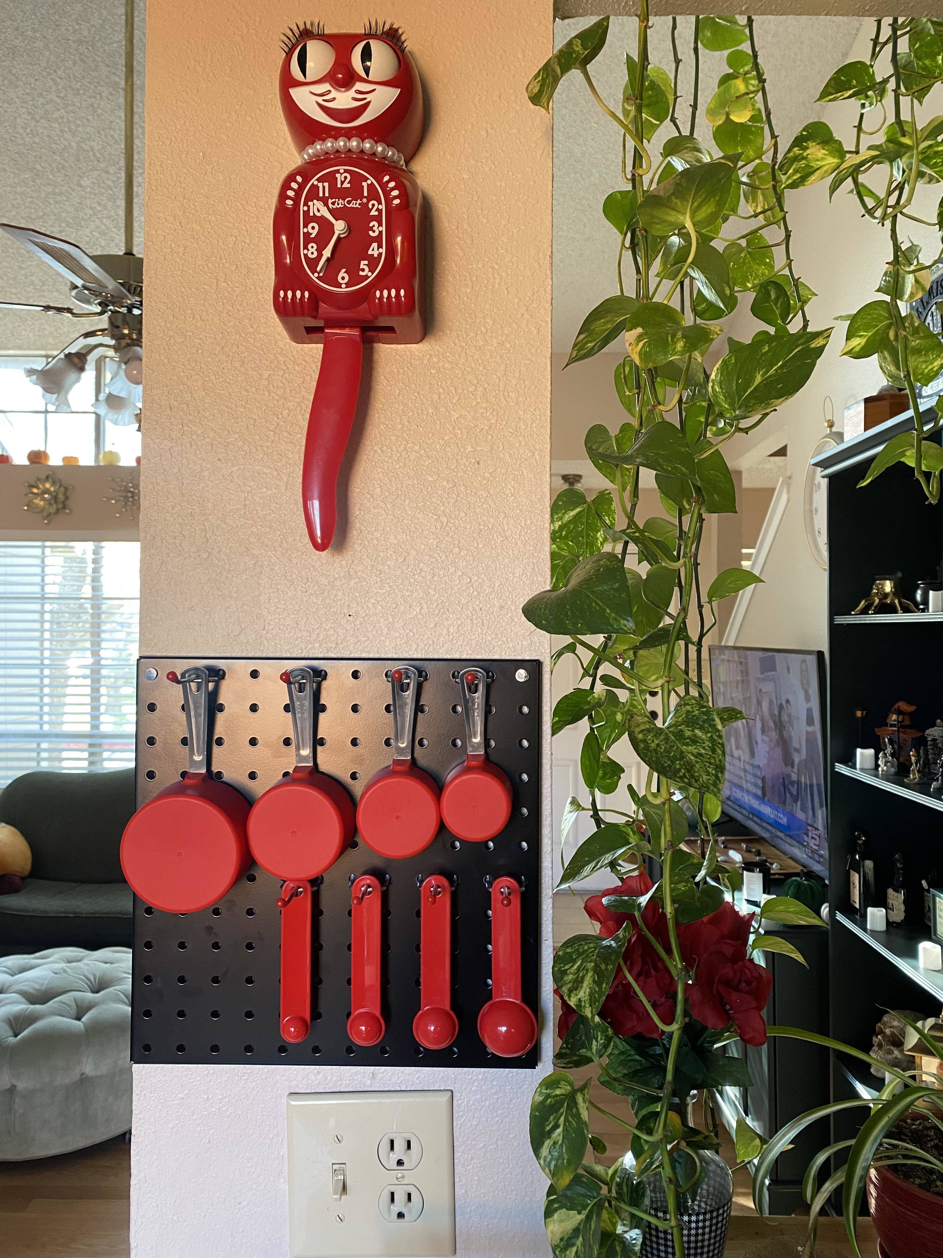 Mini pegboard on a kitchen wall holding four measuring cups and four measuring spoons