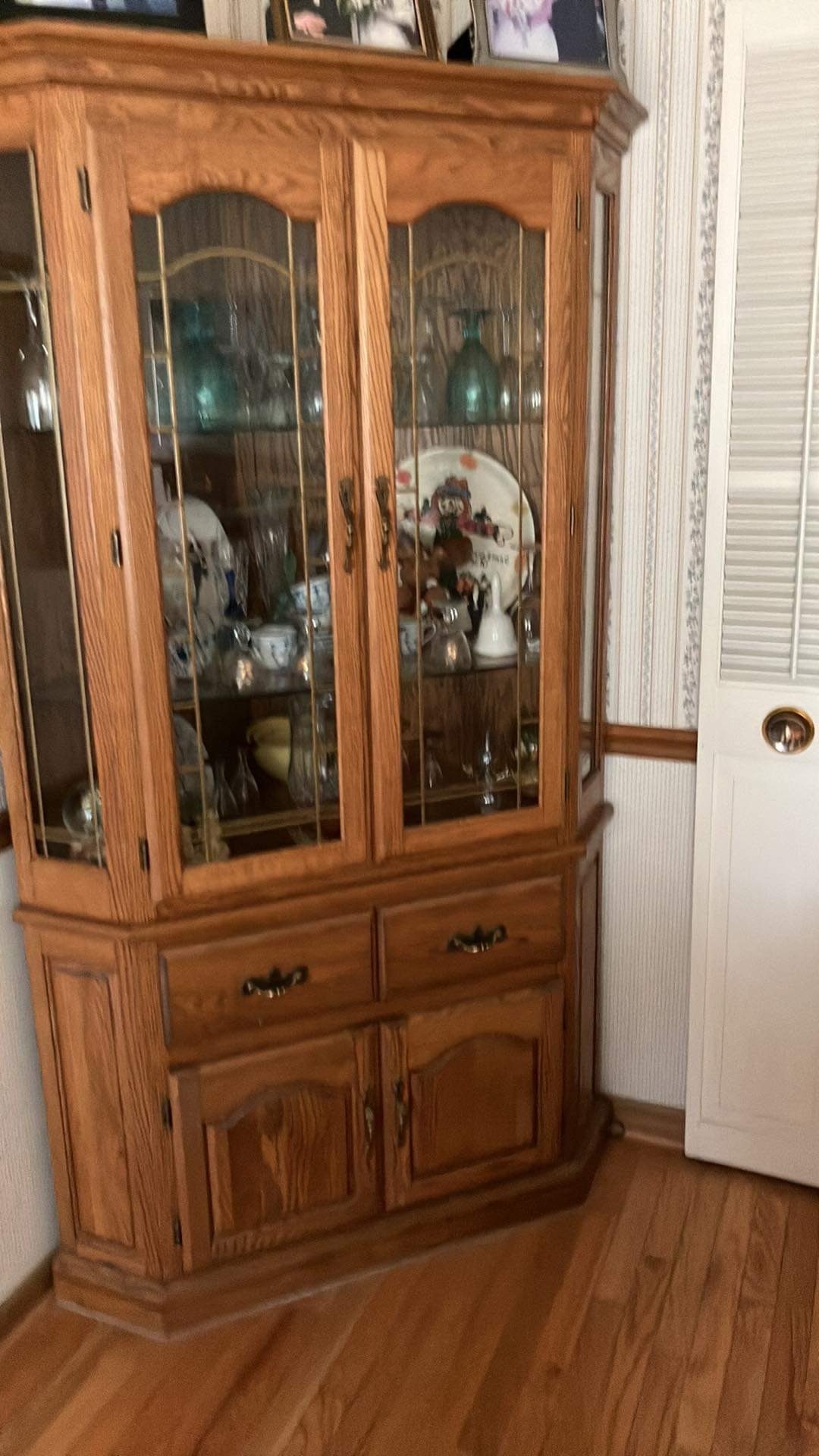 A large wooden cabinet with glass doors and containing glass figurines, glasses, and plates