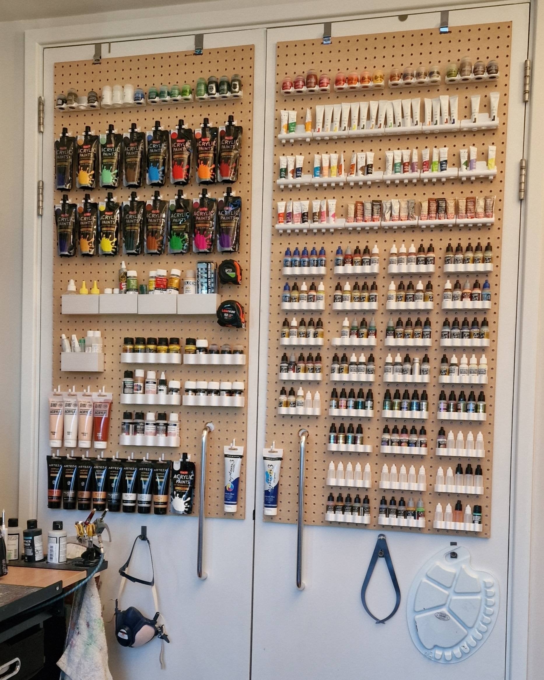 Large pegboards used to store and organize art supplies, including many paints