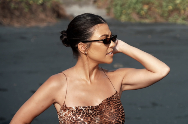 Kourtney Kardashian wears sunglasses and a swimsuit on a beach.