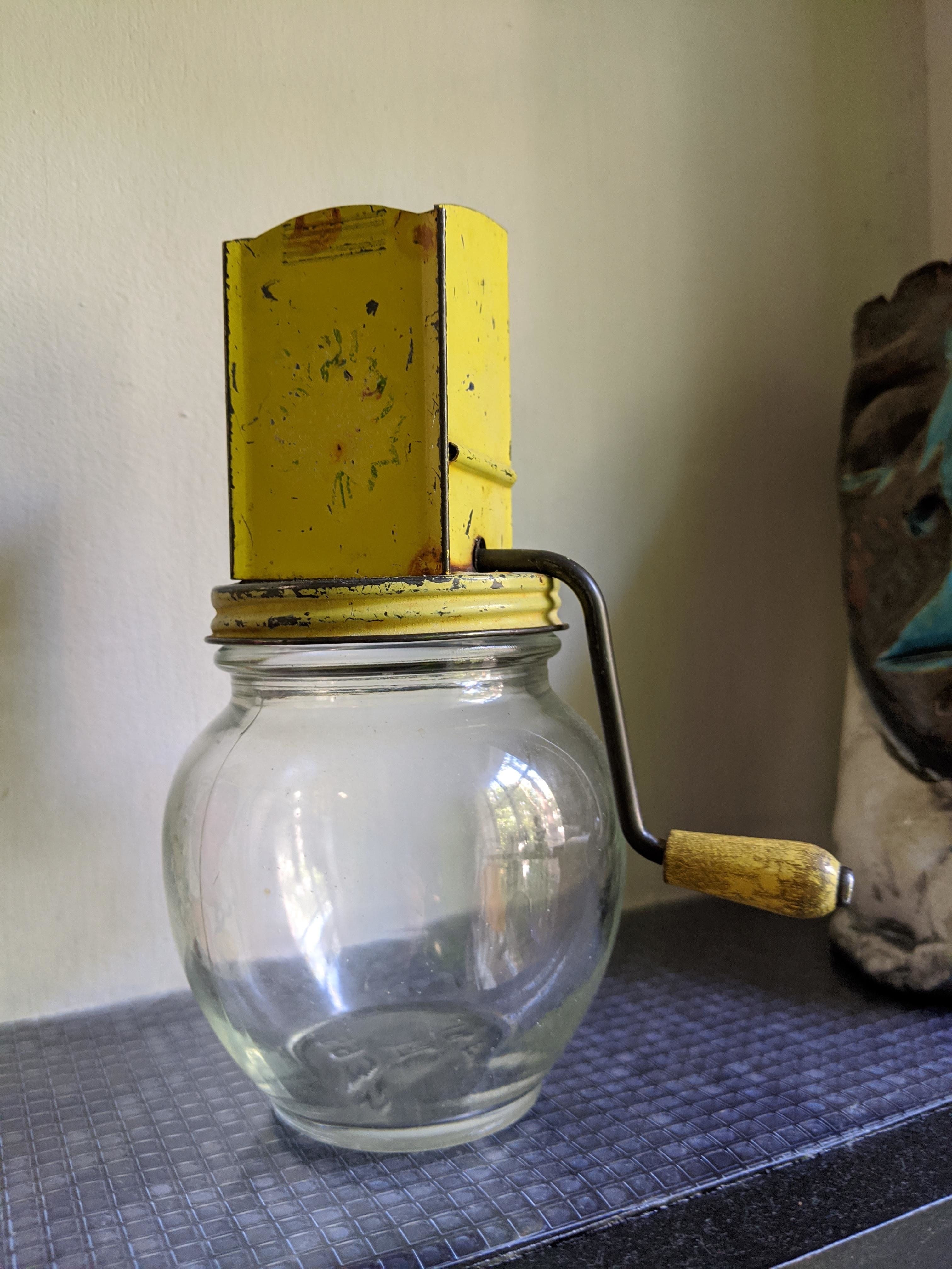 metal nut grinder with a wood handle over a glass vase for catching the ground nuts