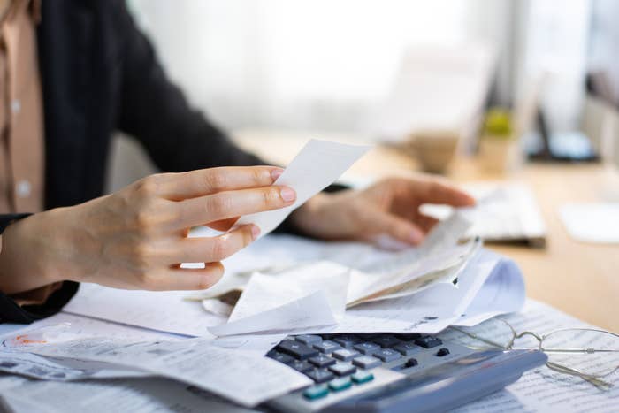 person going through a stack of papers with a calculator on their desk