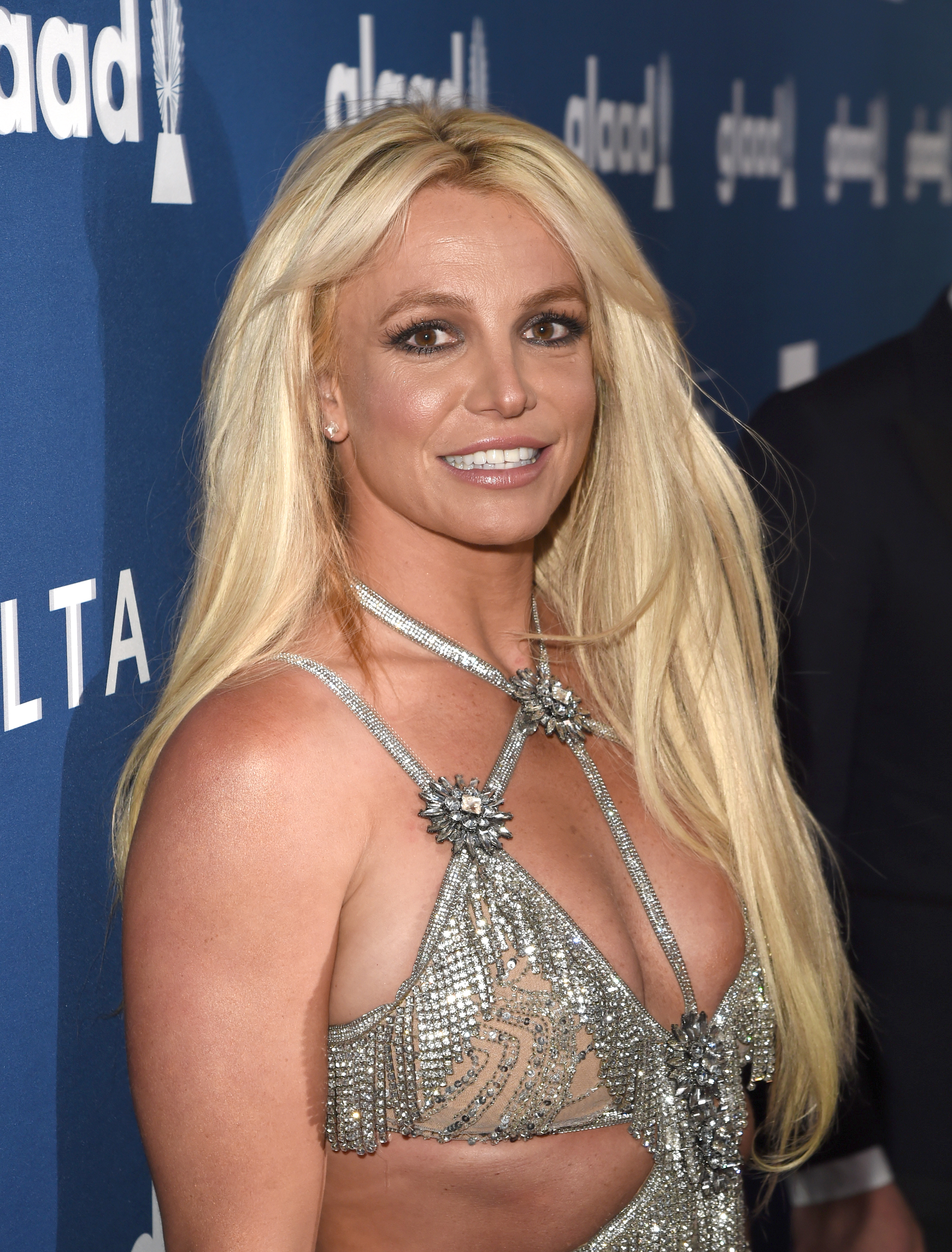 Close-up of Britney smililng at a media event and wearing a sparkly cutout outfit