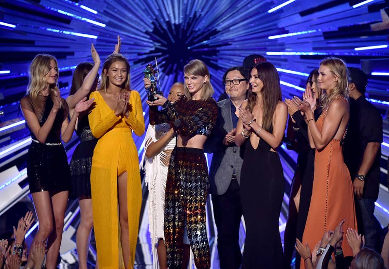 Close-up of Taylor onstage holding up an award with many other people