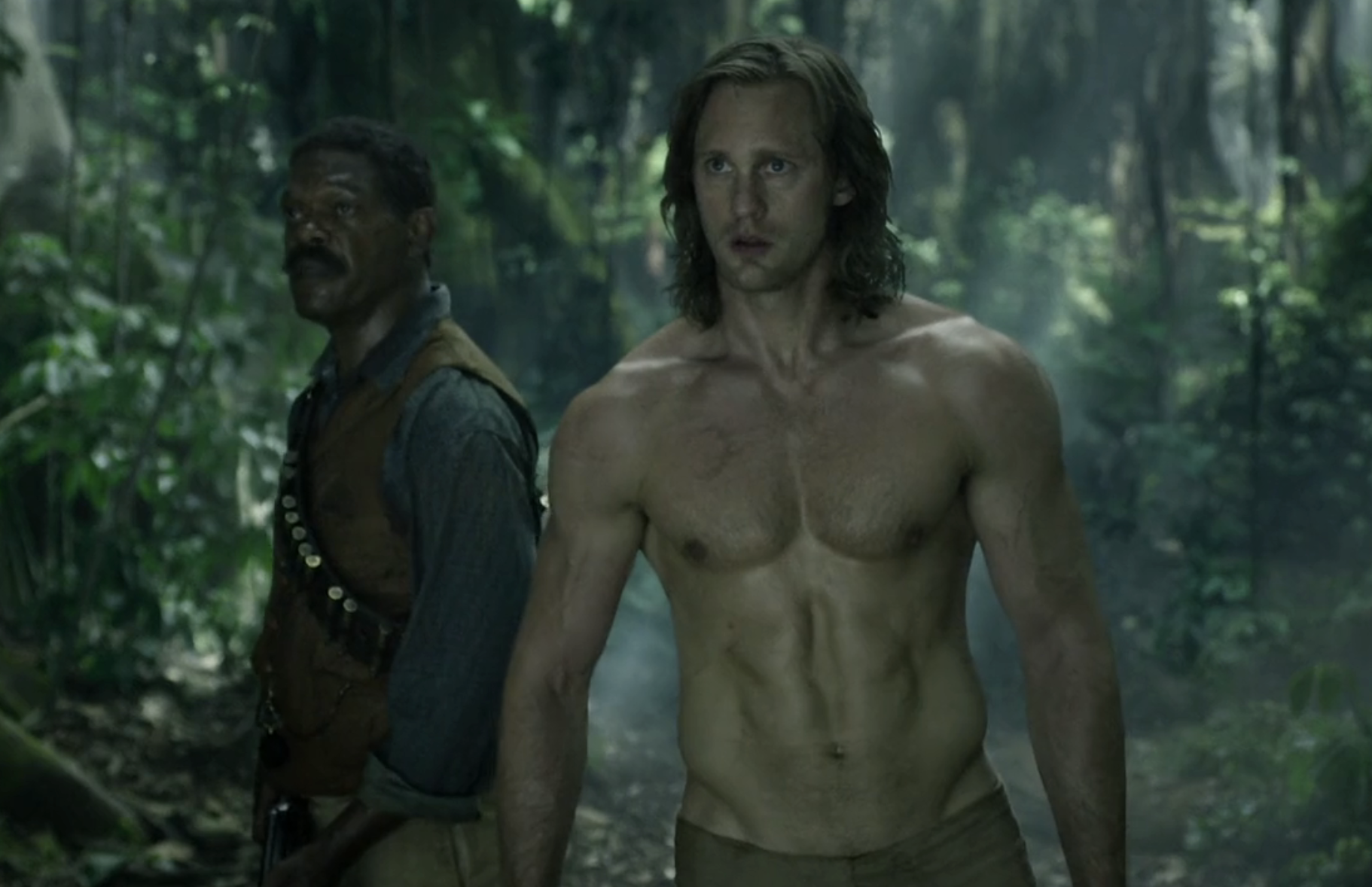 Alexander shirtless in the jungle, standing next to Samuel L. Jackson&#x27;s character