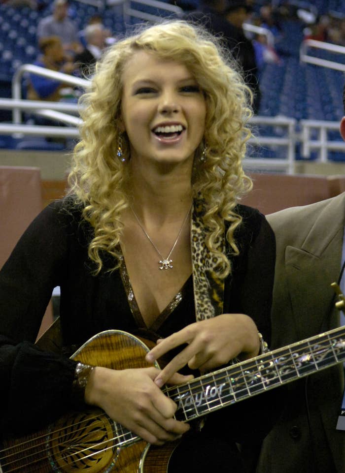 A close-up of a younger Taylor smiling and holding a guitar