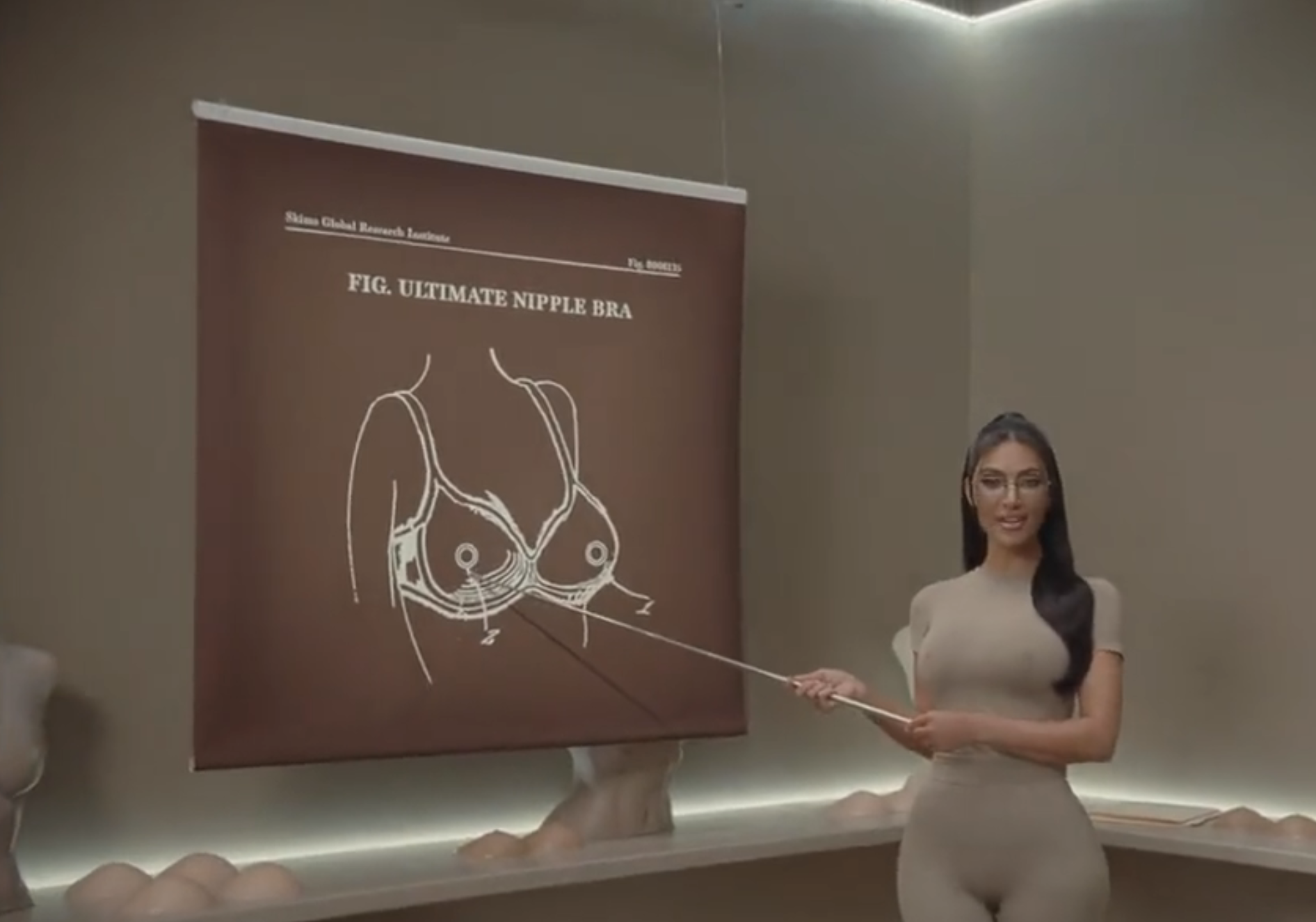 kim pointing to a drawing of a bra