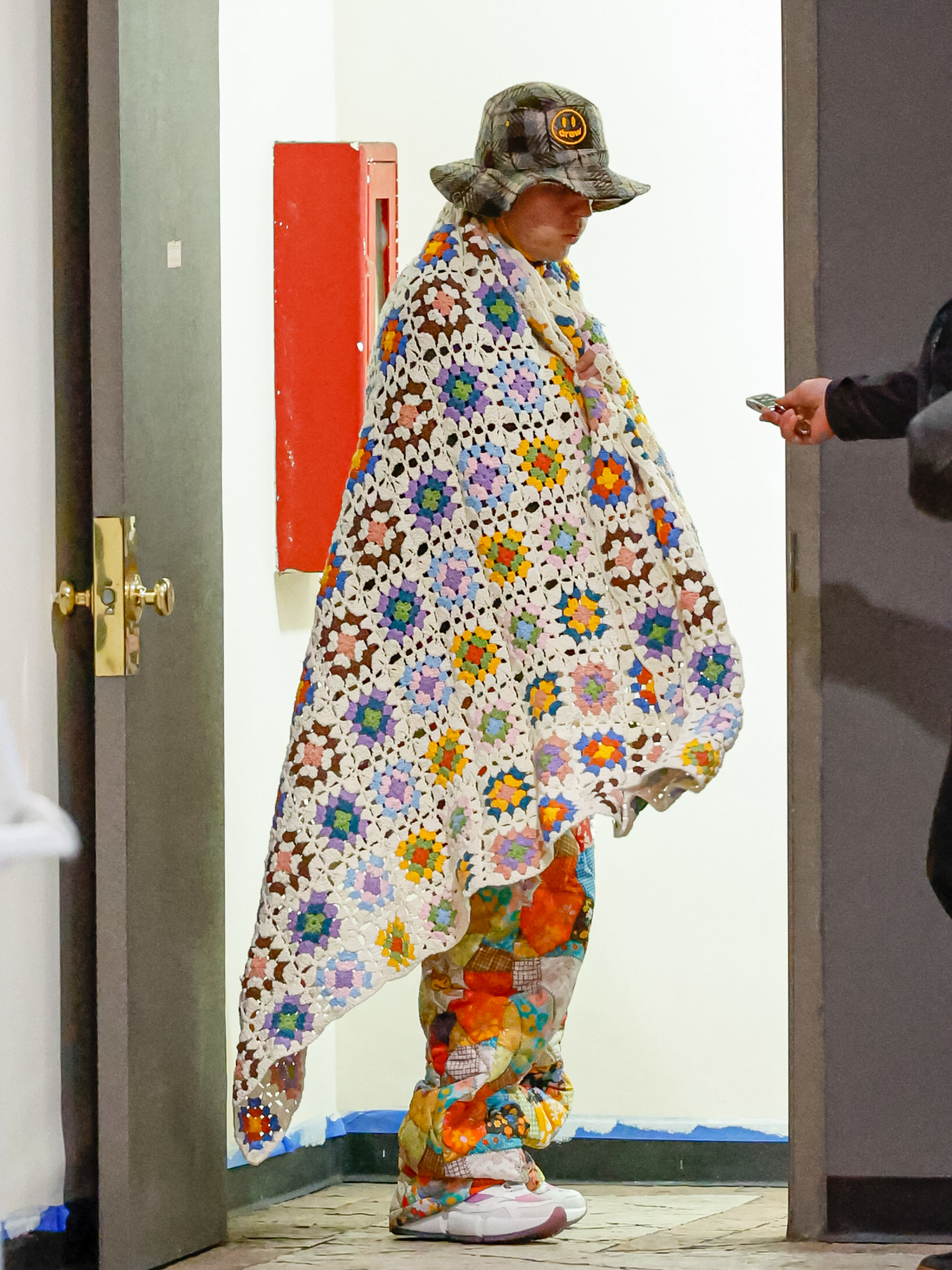he's wearing the blanket over patchwork pants and he's also wearing a bucket hat