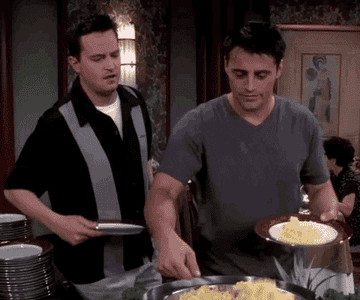 Joey from Friends scoops a massive amount of egg onto his plate as Chandler watches.