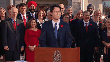 Justin Trudeau opens his arms up and shakes his head in front of a podium.