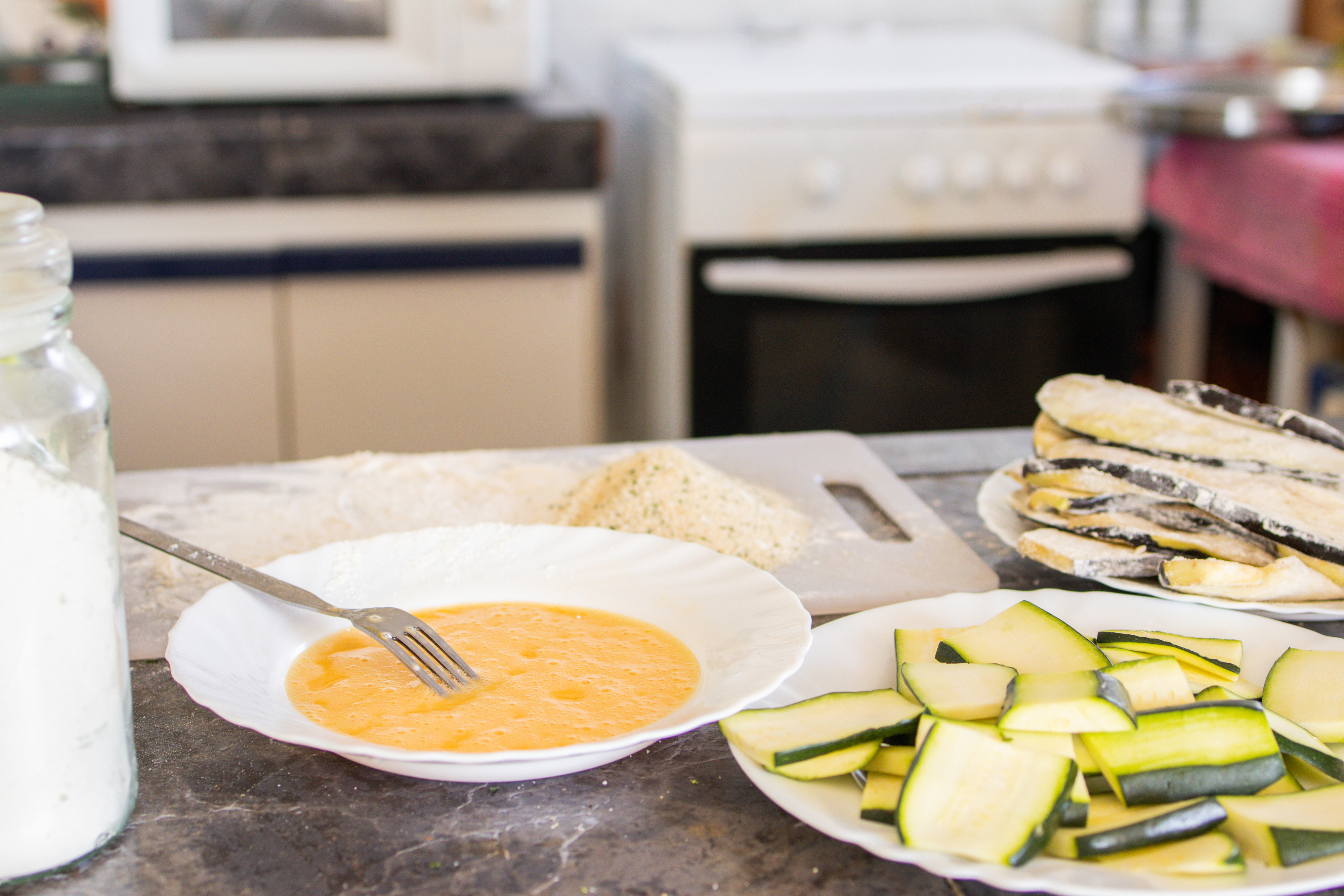 a shallow bowl of batter and a plate of zucchini slices