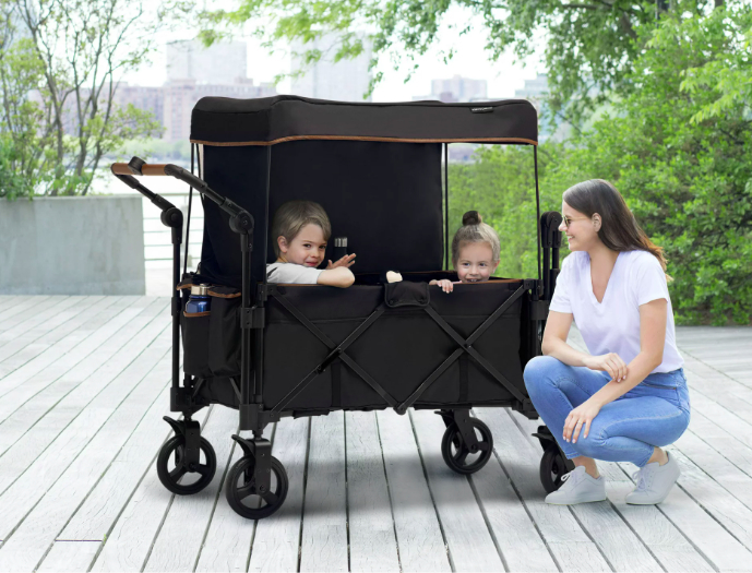 A woman kneeling in front of the wagon, which has two children inside