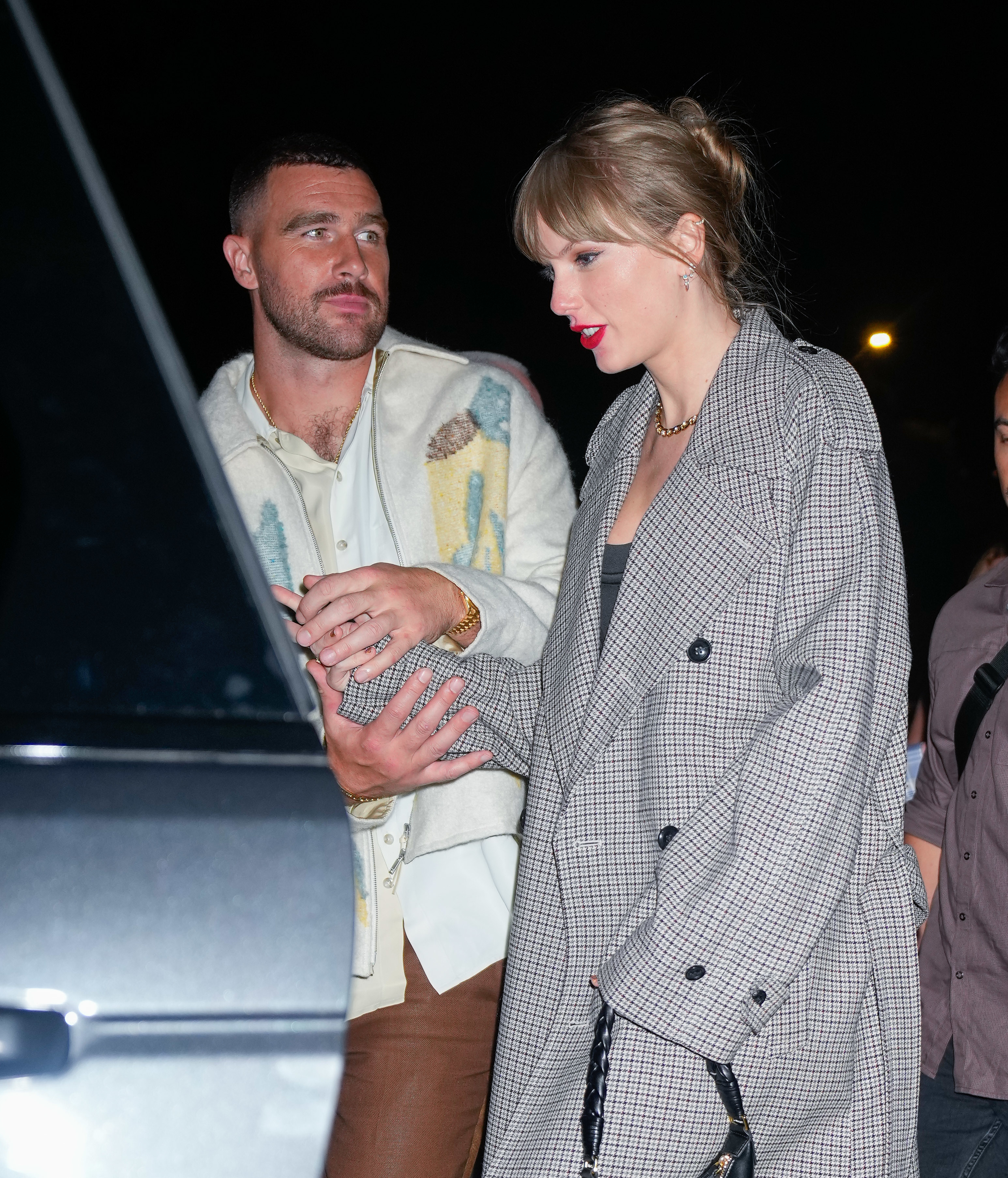 Close-up of Taylor and Travis standing in front of a car and Travis holding her hand in both of his
