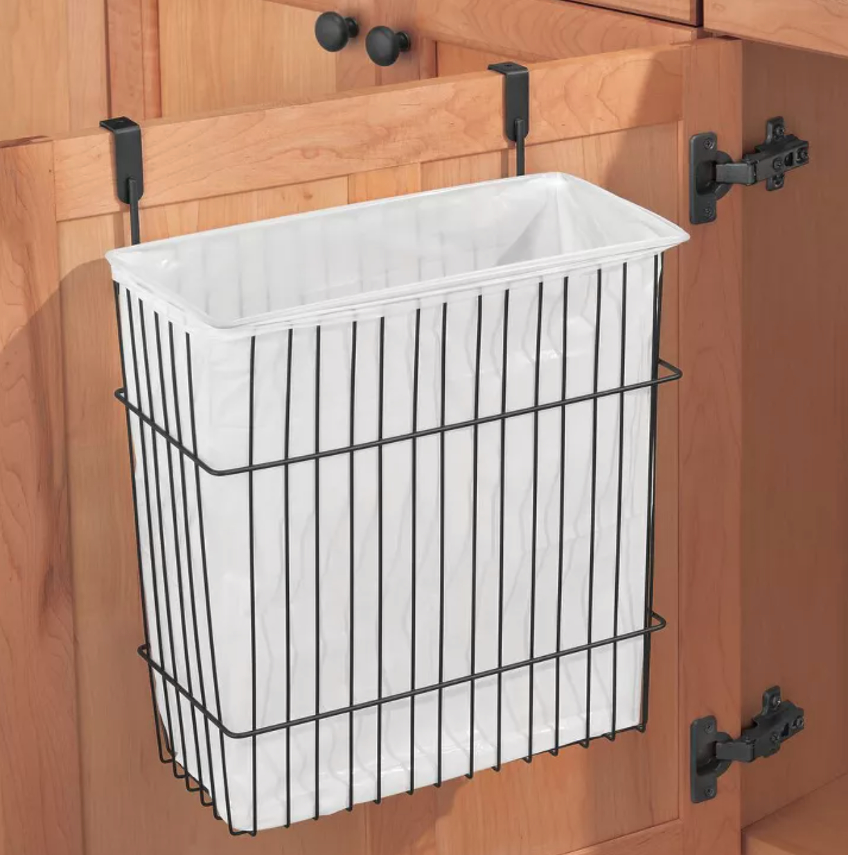 a wire basket filled with a plastic bag for trash hanging over a cabinet door