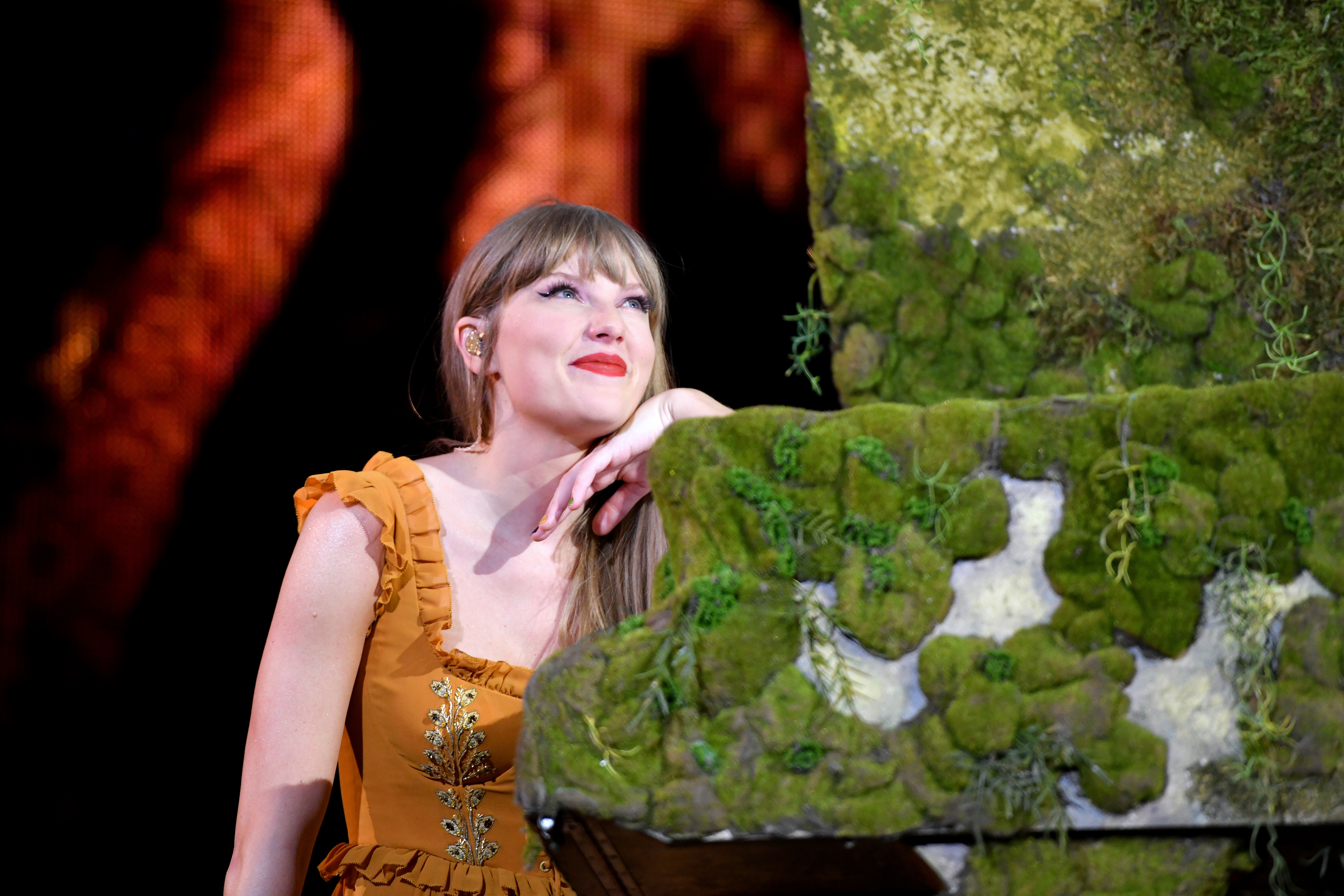 Close-up of Taylor smiling and leaning on a mossy surface as she looks up