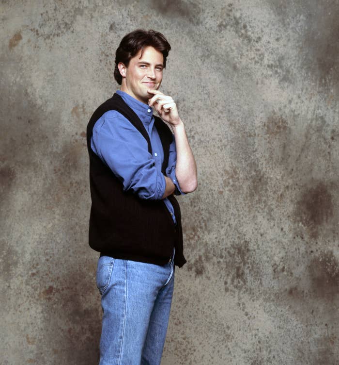 Close-up of a young Matthew standing and posing and wearing a shirt, vest, and jeans