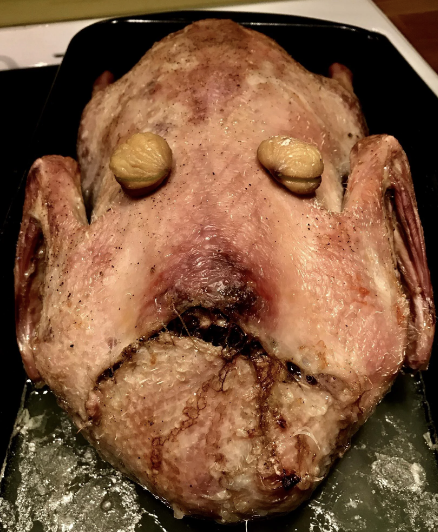A ham or turkey has been placed on a pan, with walnuts placed on it to resemble eyes; a gash in the meat makes it resemble a face that is bleeding from the mouth