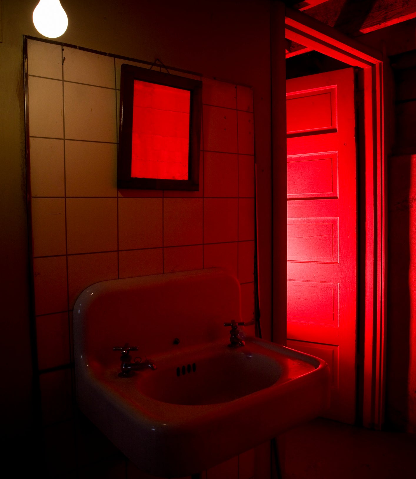 A bathroom sink is bathed in an eerie red light