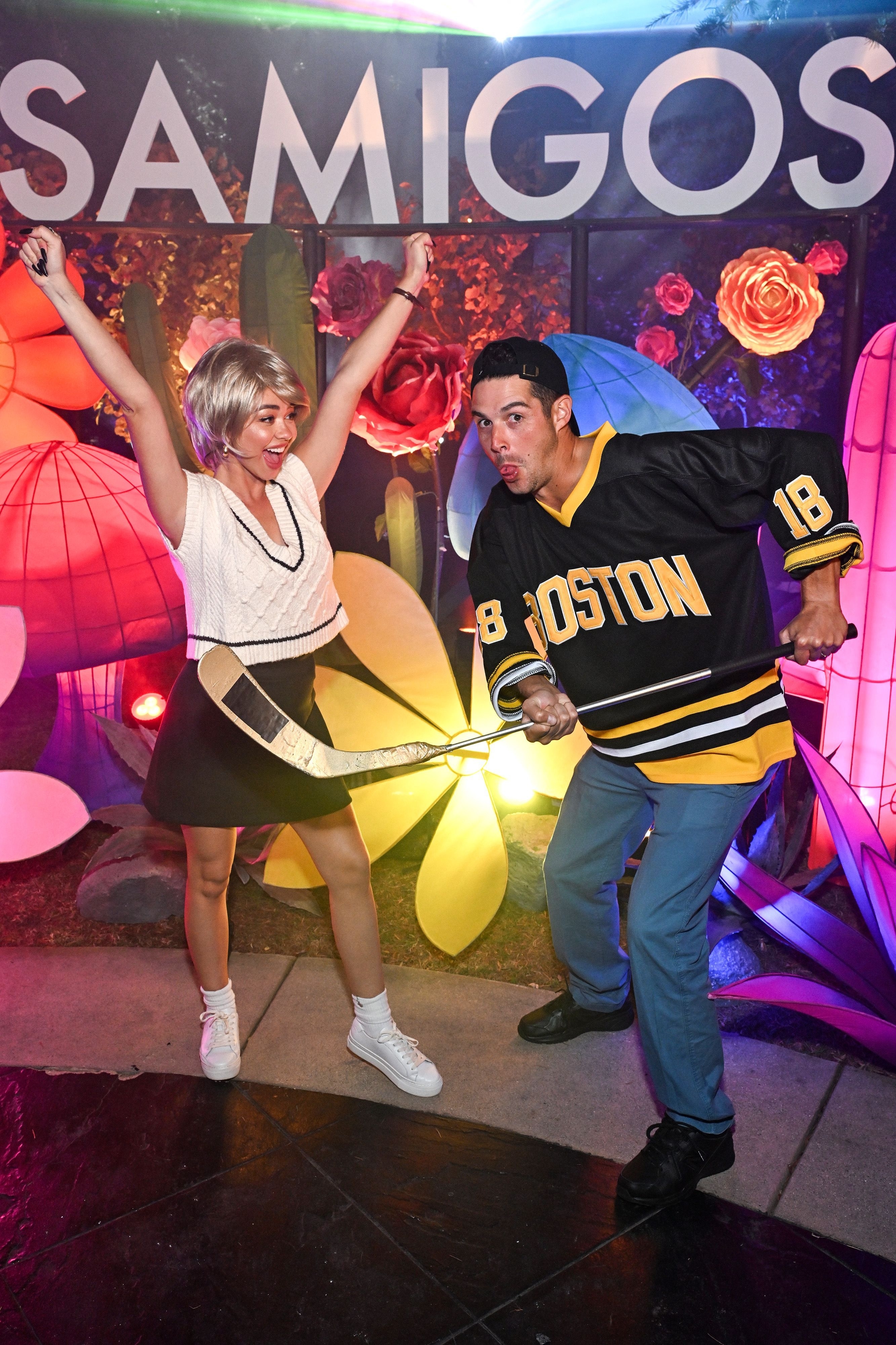 she cheers in a short blonde wig as he holds a hockey stick