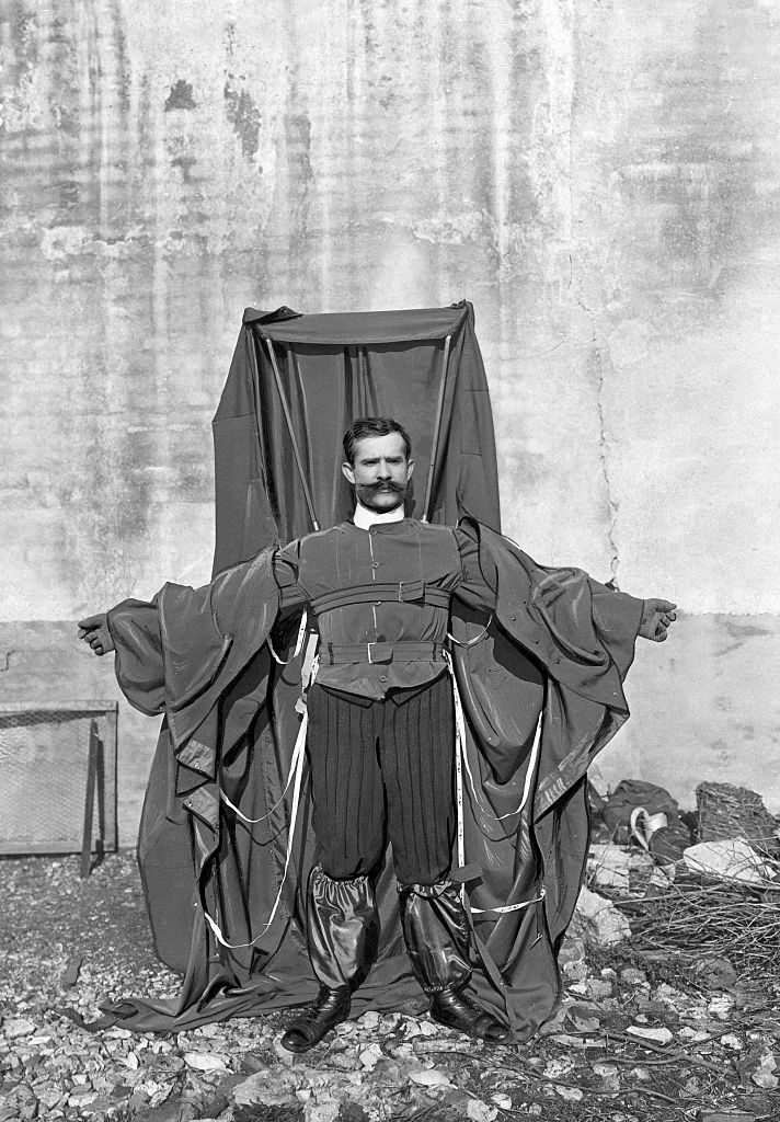 A man in a black-and-white photo with a large piece of cloth attached to his suit with several straps