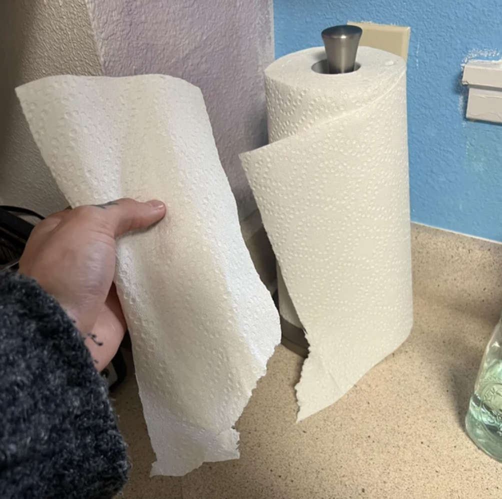 person tearing a paper towel off the roll but it&#x27;s ripped near the bottom so part of the sheet remains on the roll