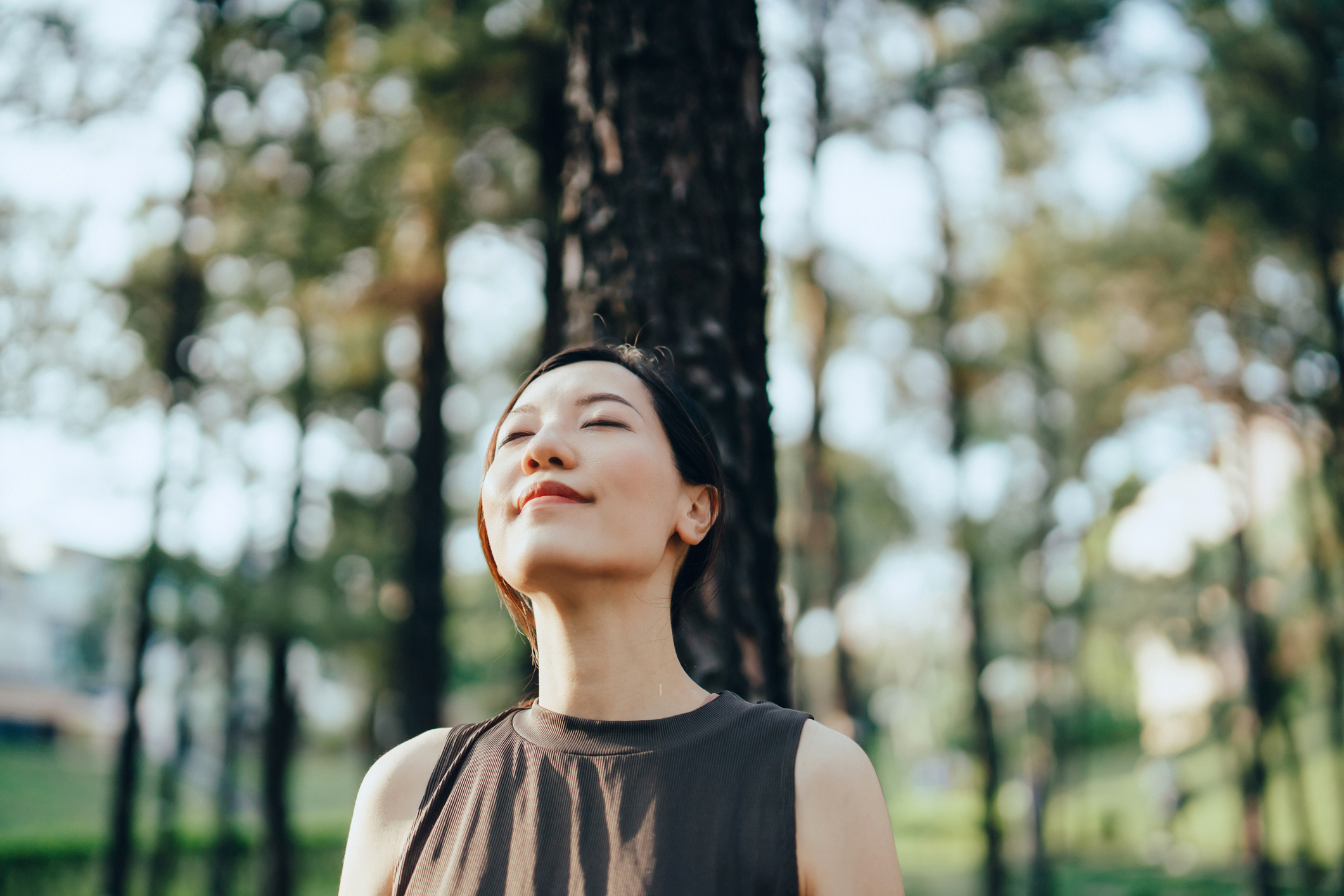A woman smiling with her eyes closed while standing in the sun