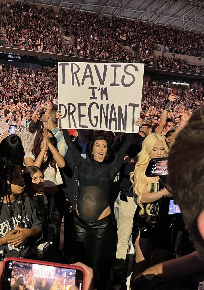 a pregnant kourtney in the crowd holding a sign that says, &quot;travis i&#x27;m pregnant&quot;