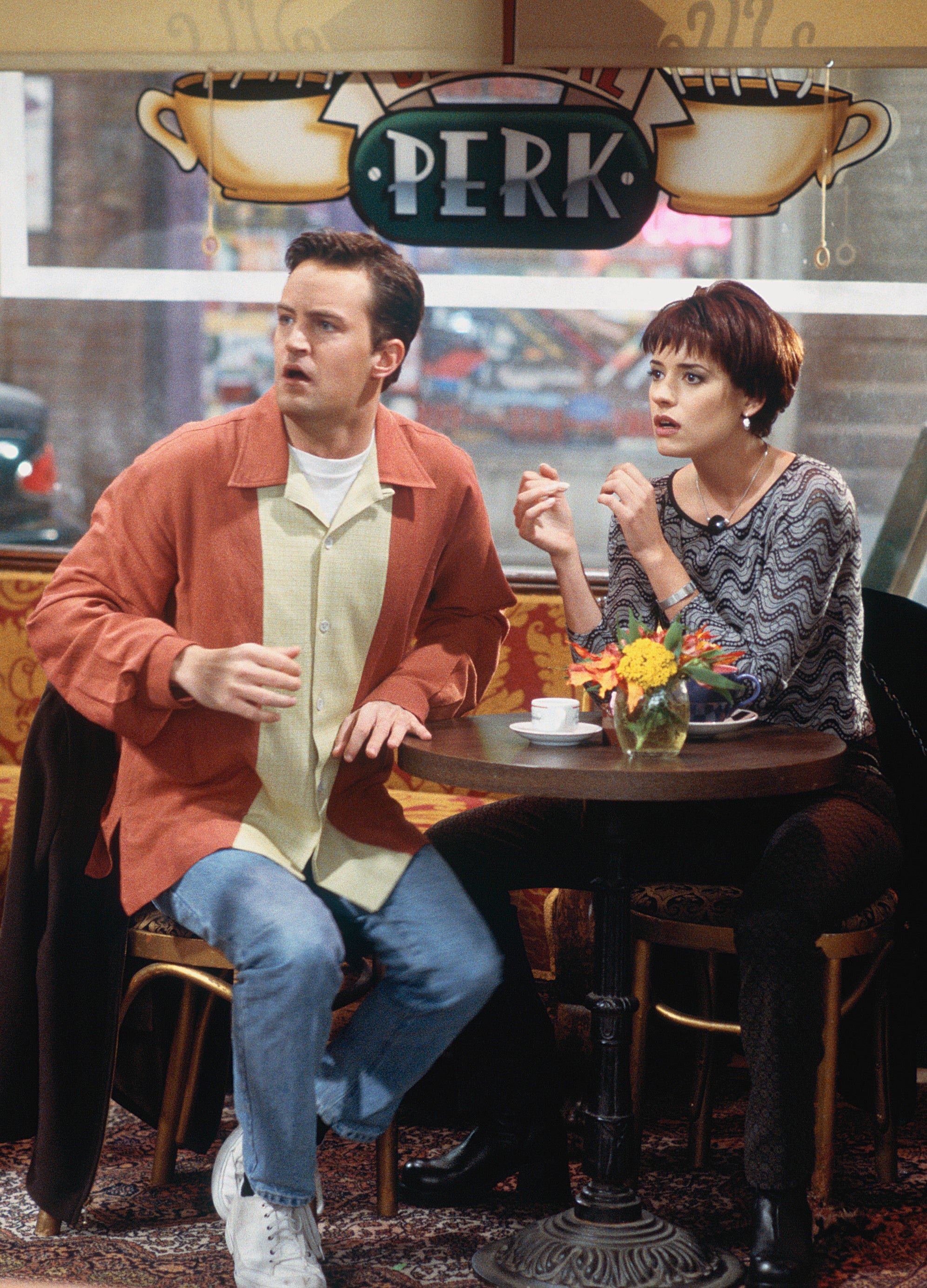 Paget Brewster and Matthew sitting at a table in a coffee shop in a scene from &quot;Friends&quot;