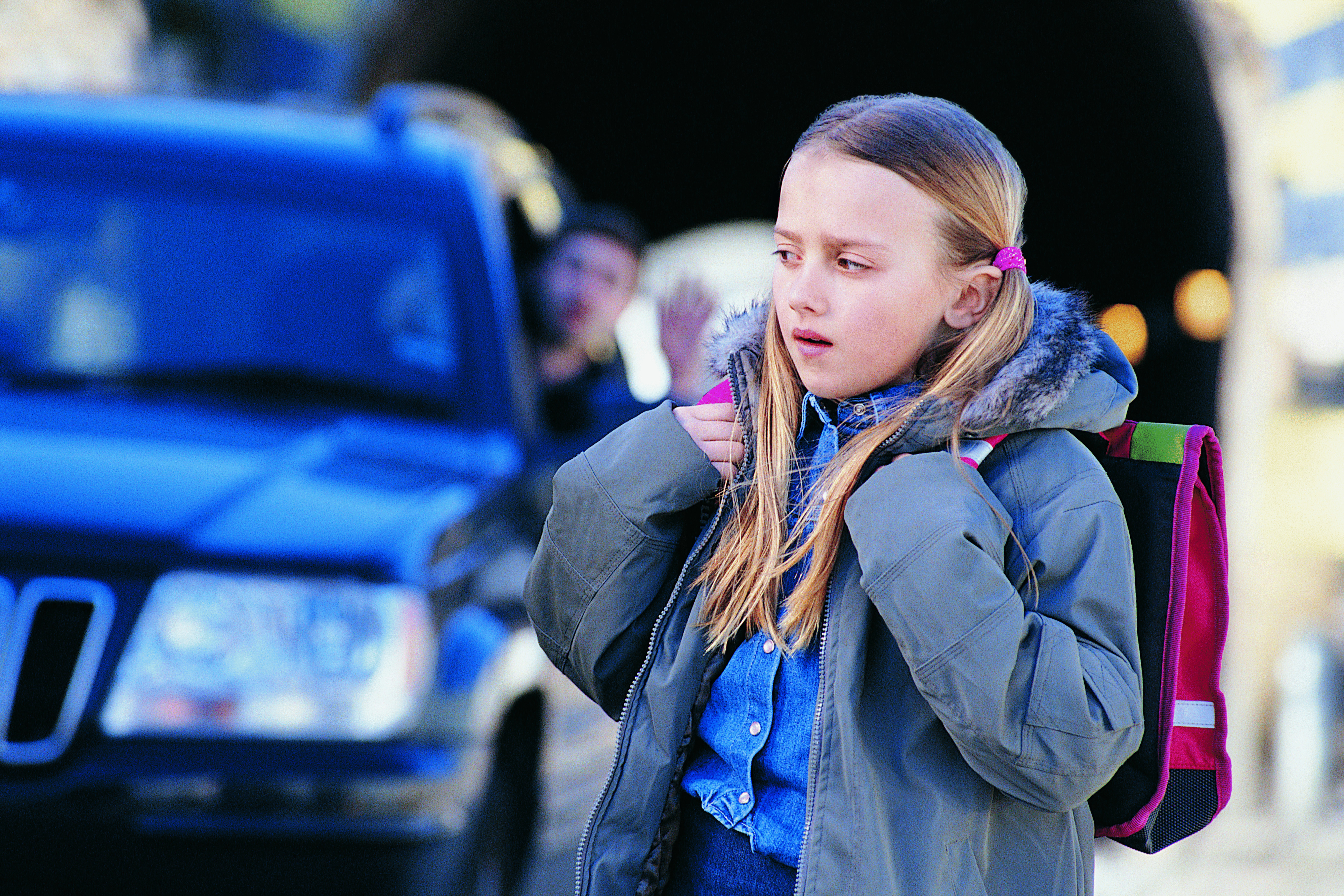 a kid walking down the street with a scared look while a car follows behind them