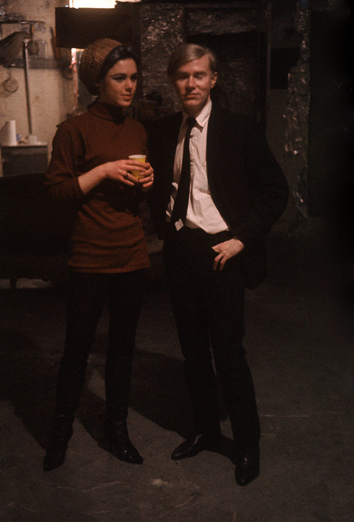 he's wearing a suit with a skinny tie and she's wearing a turtle neck and leggings