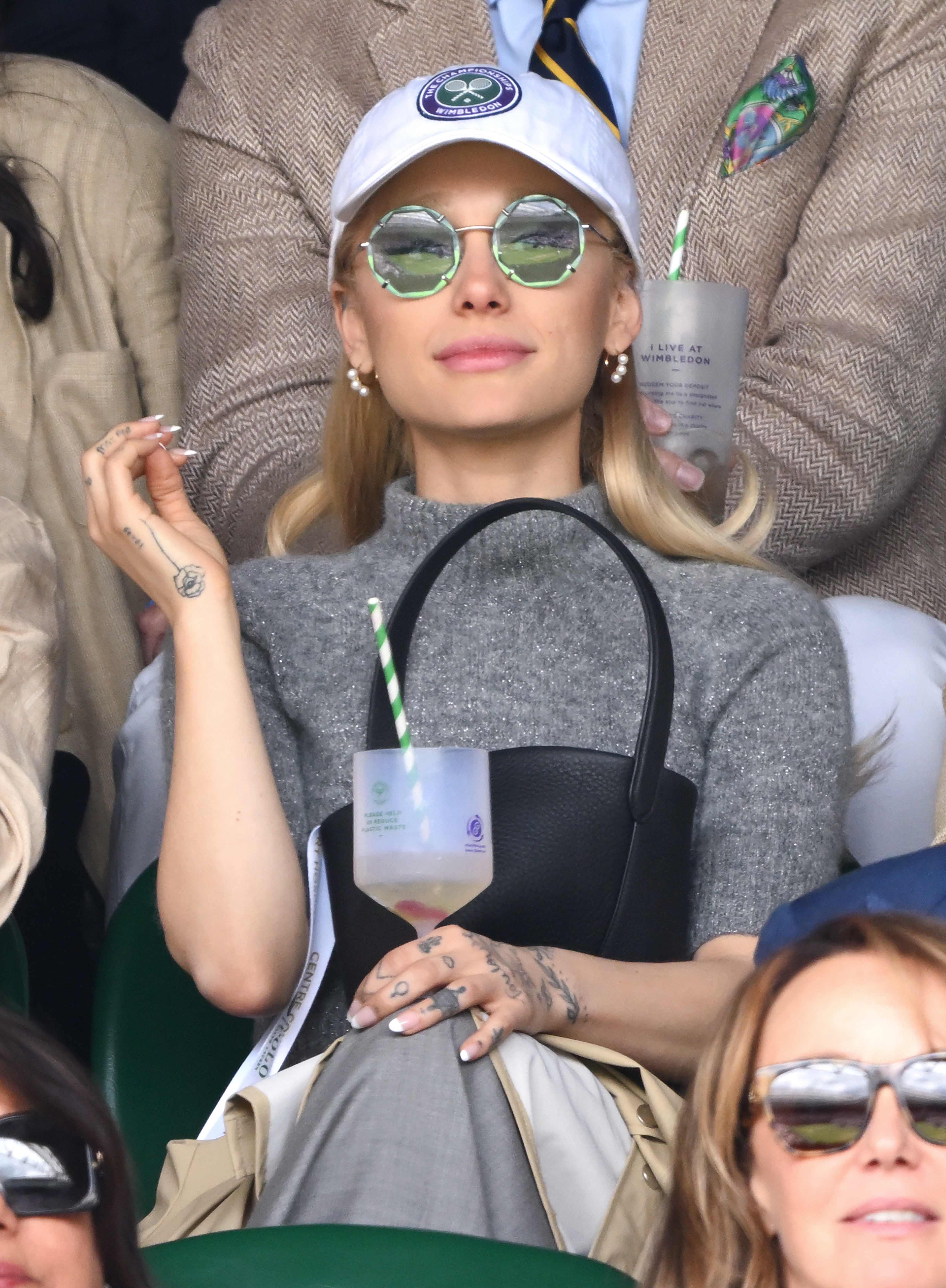 Closeup of Ariana Grande holding a drink as she sits in the stands