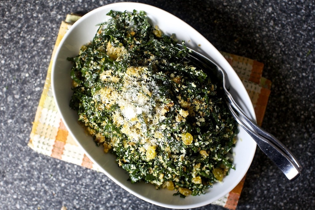 large bowl of kale salad topped with cheese, breadcrumbs, and raisins