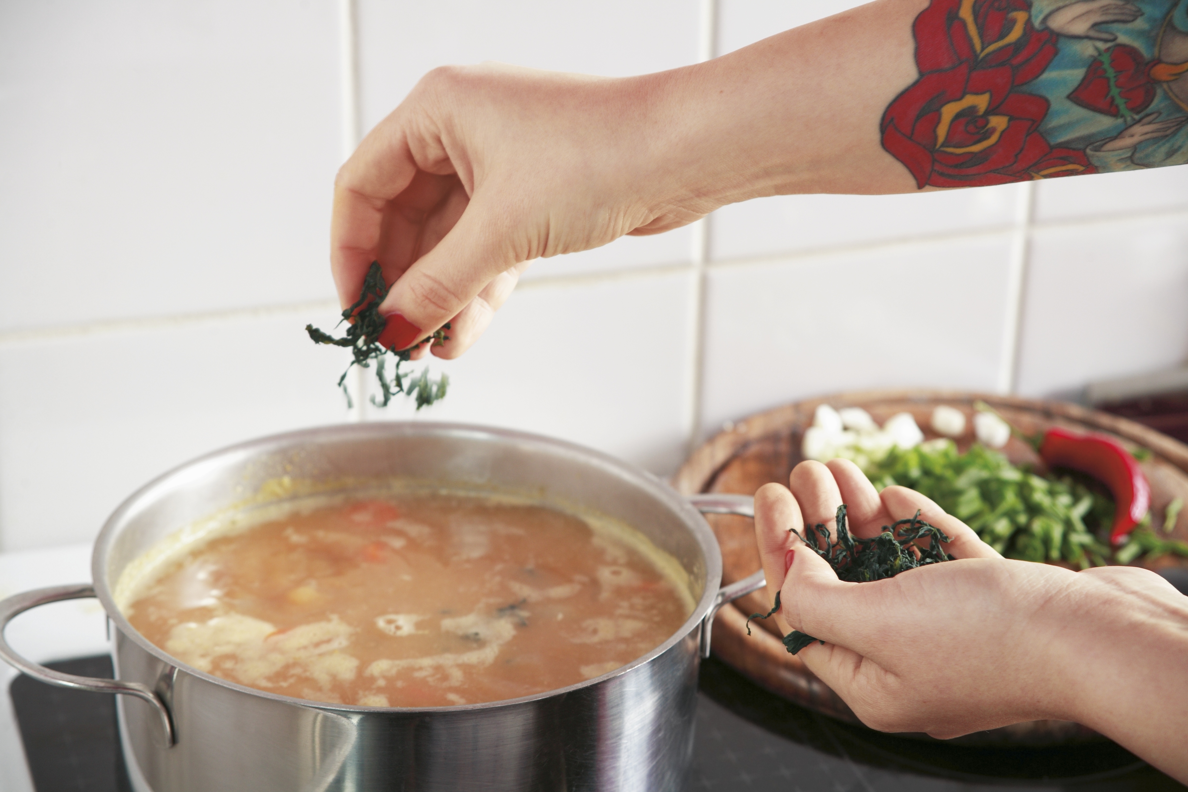 woman adding herbs to a pot of soup